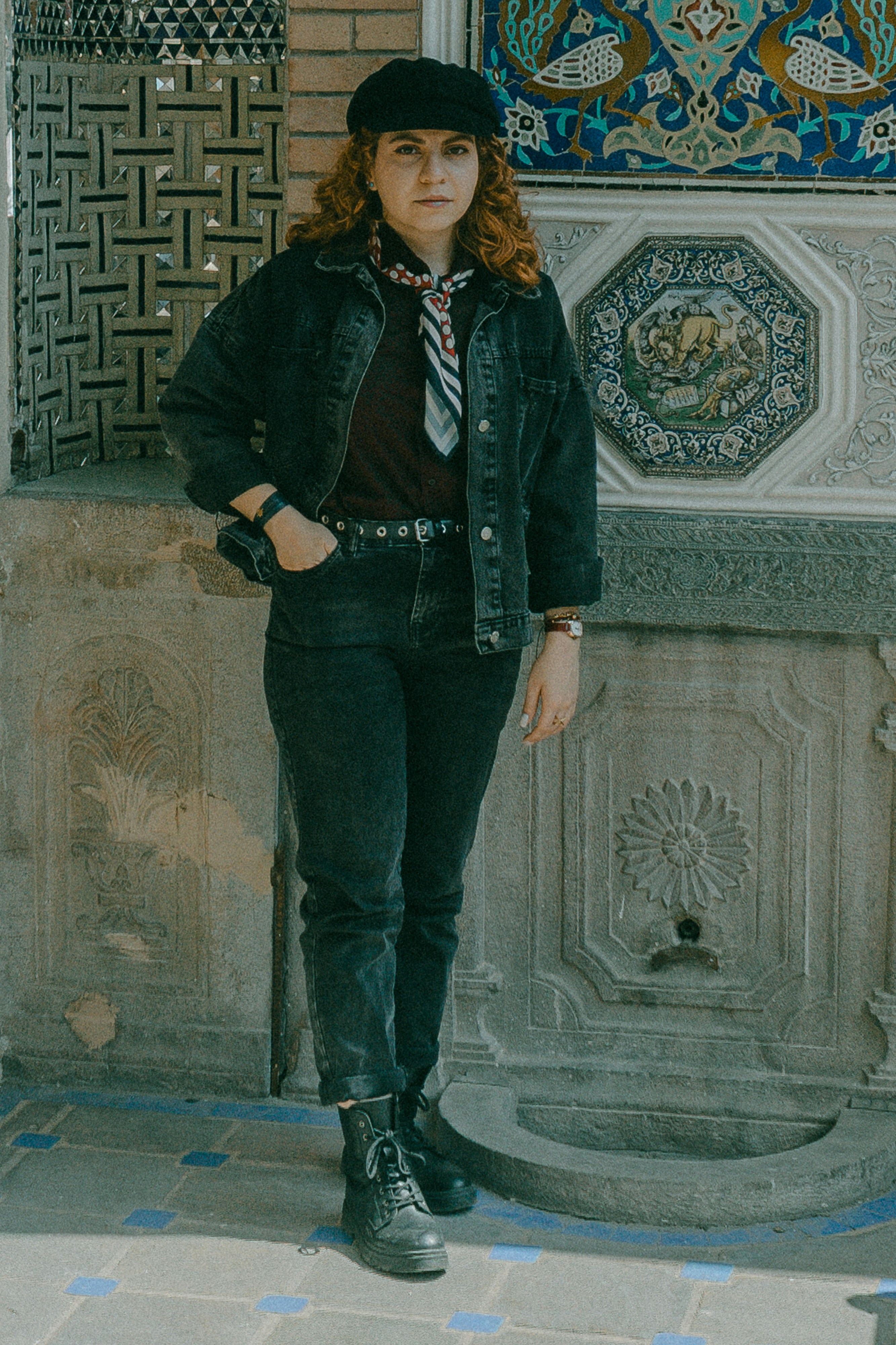 A woman in a black denim jacket and jeans standing before an ornate tiled wall