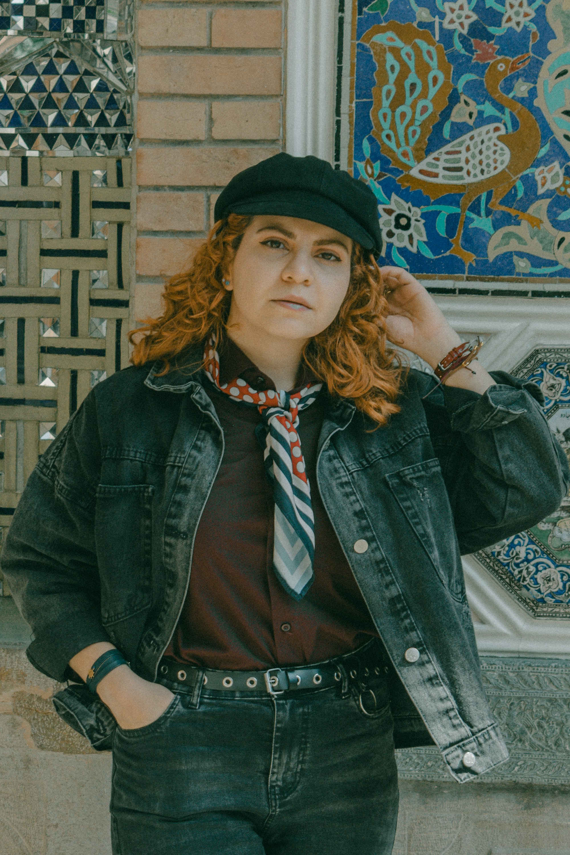 A person with curly red hair wearing a black cap and denim jacket