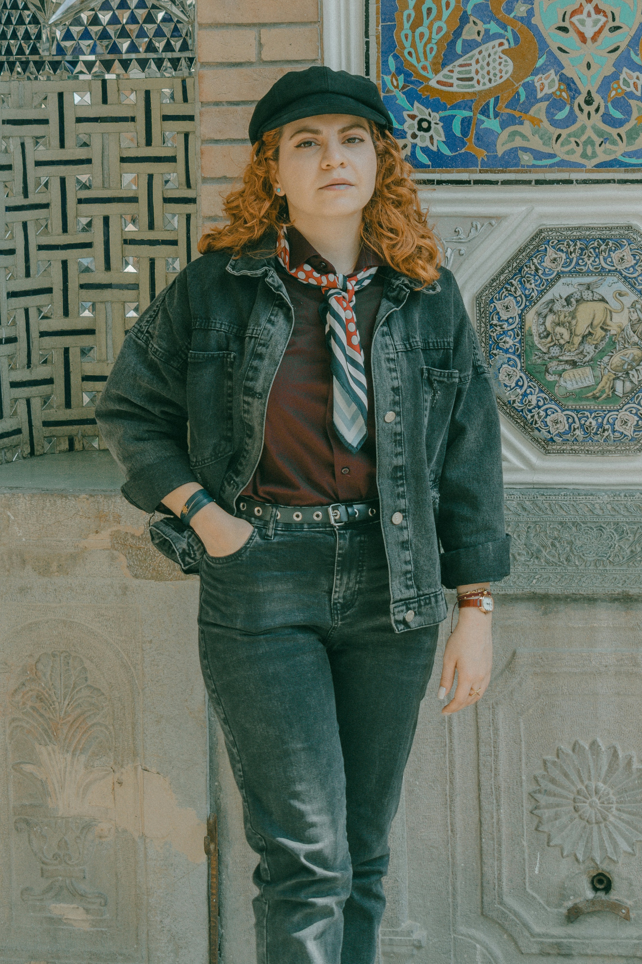 A woman with red hair wearing a black cap and denim jacket