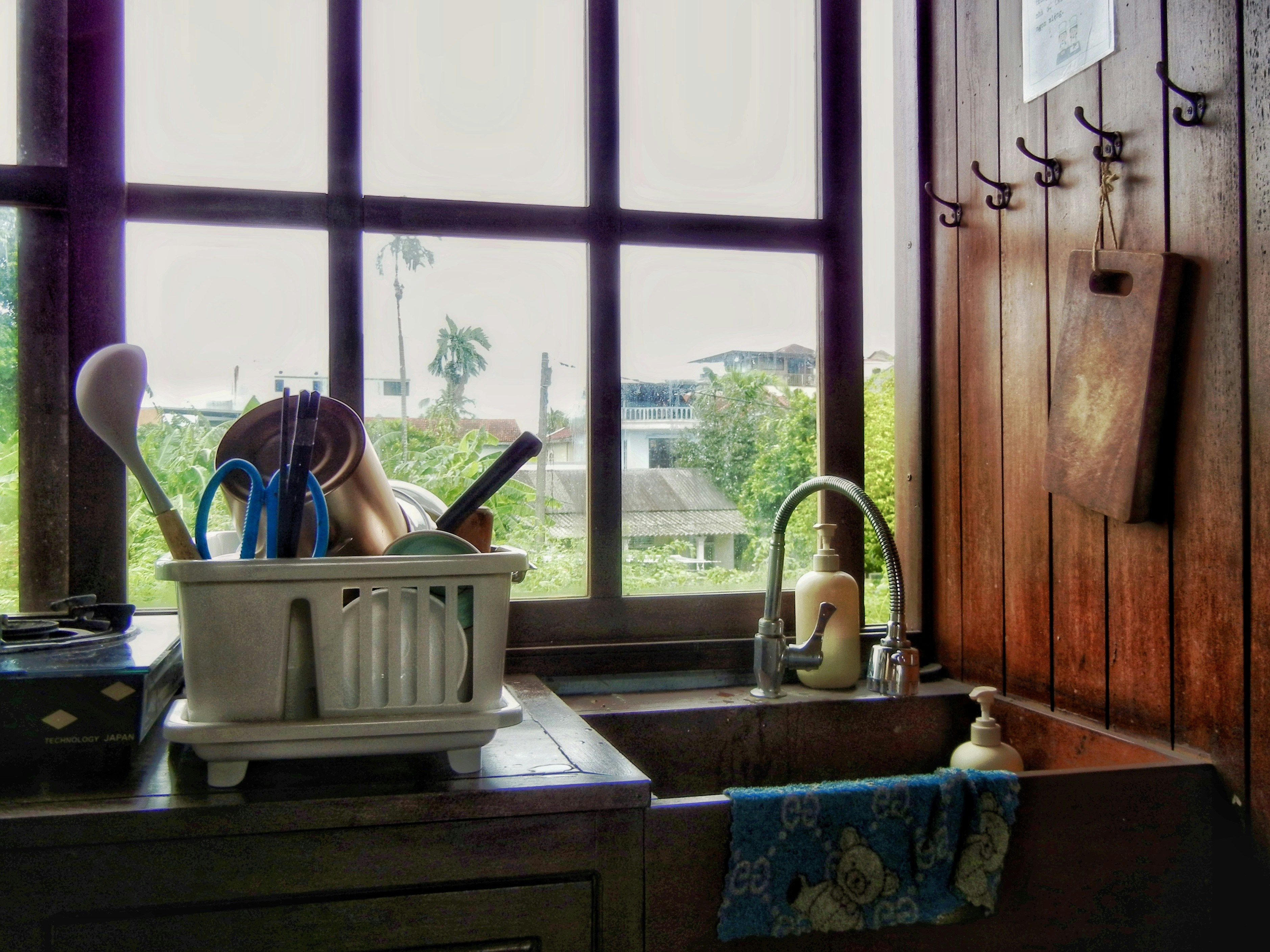 Rak piring dengan peralatan makan di samping wastafel dapur di depan jendela