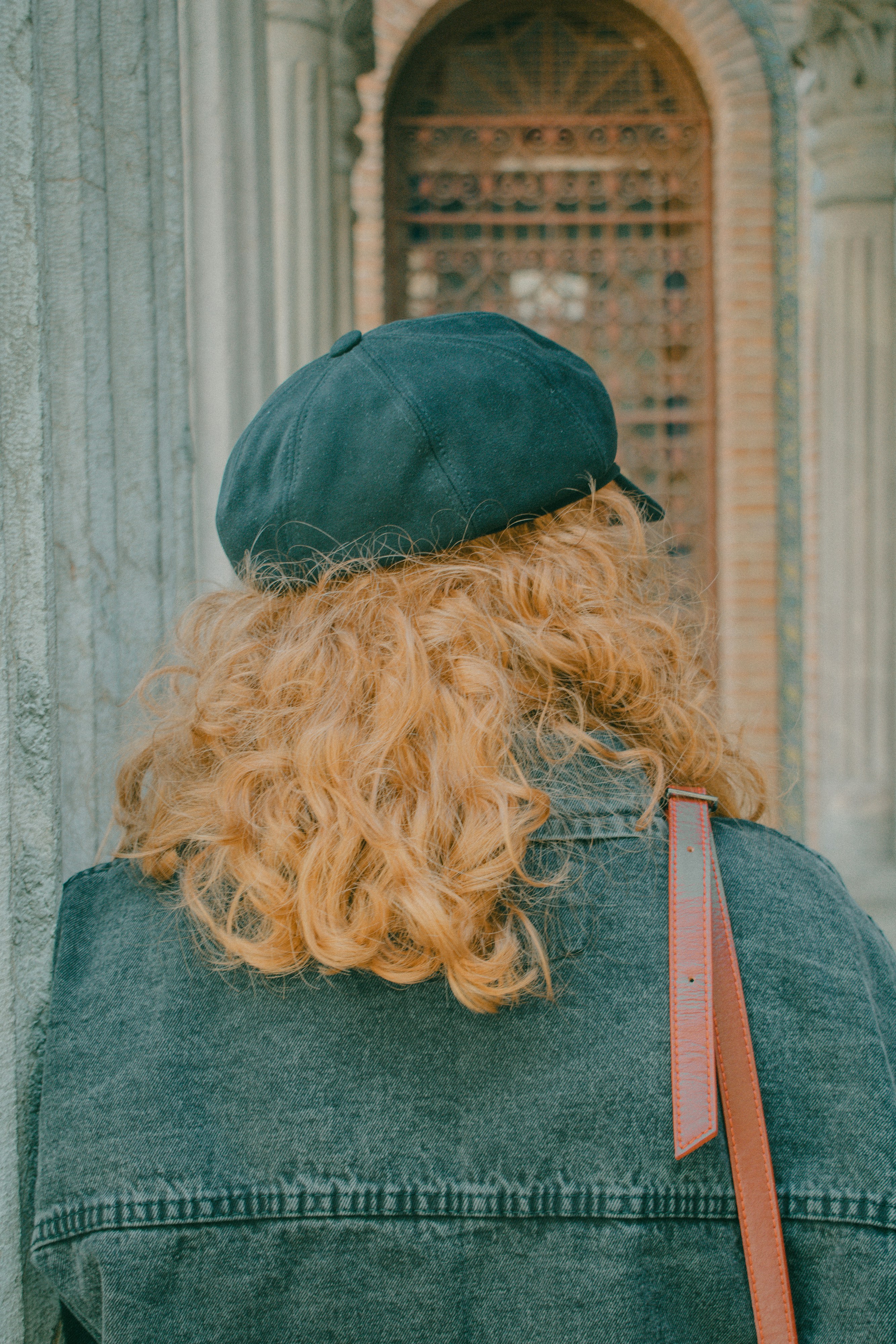 A person with curly ginger hair wearing a dark cap and denim jacket
