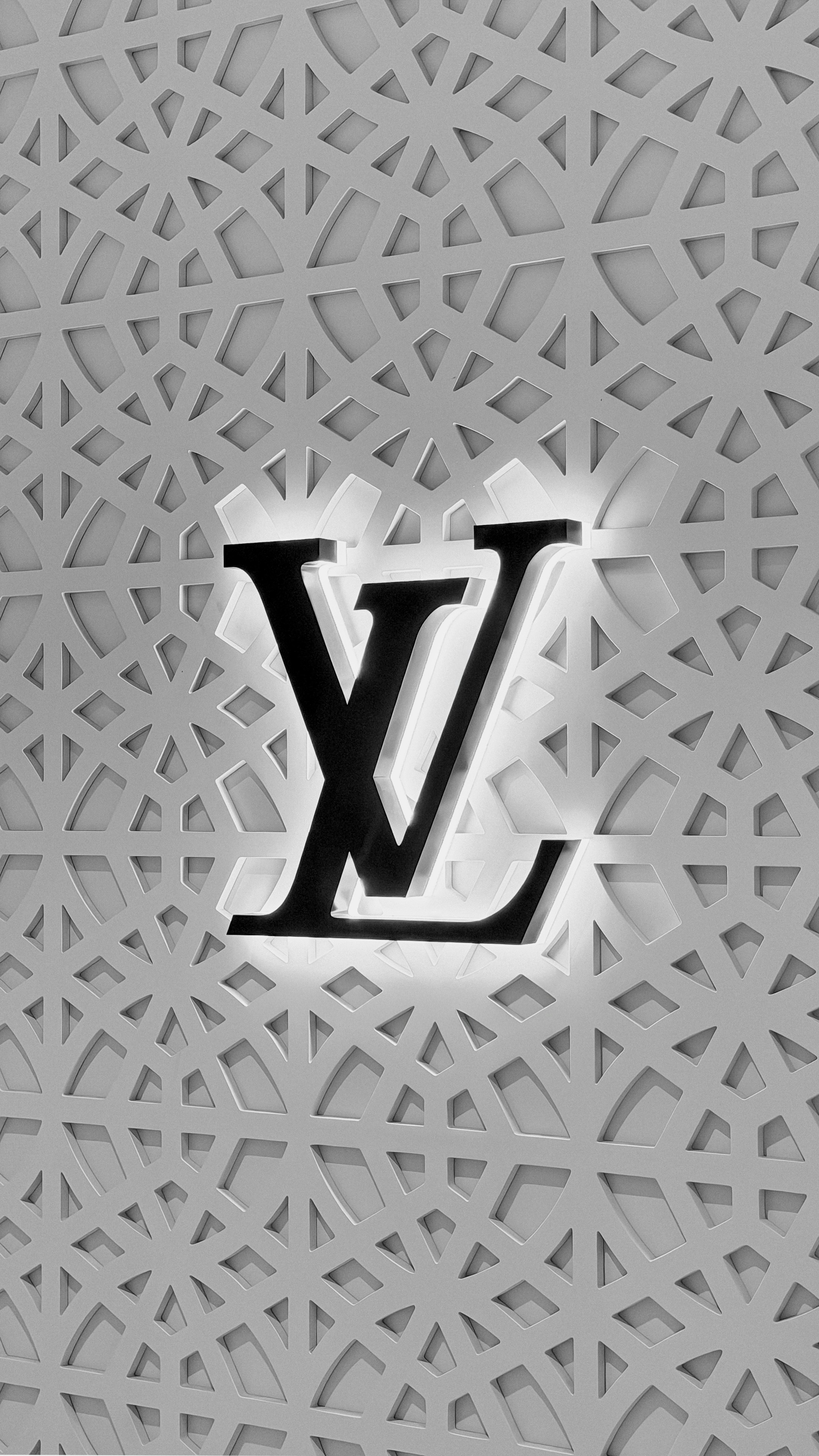 A backlit Louis Vuitton logo mounted on a grey geometric patterned wall