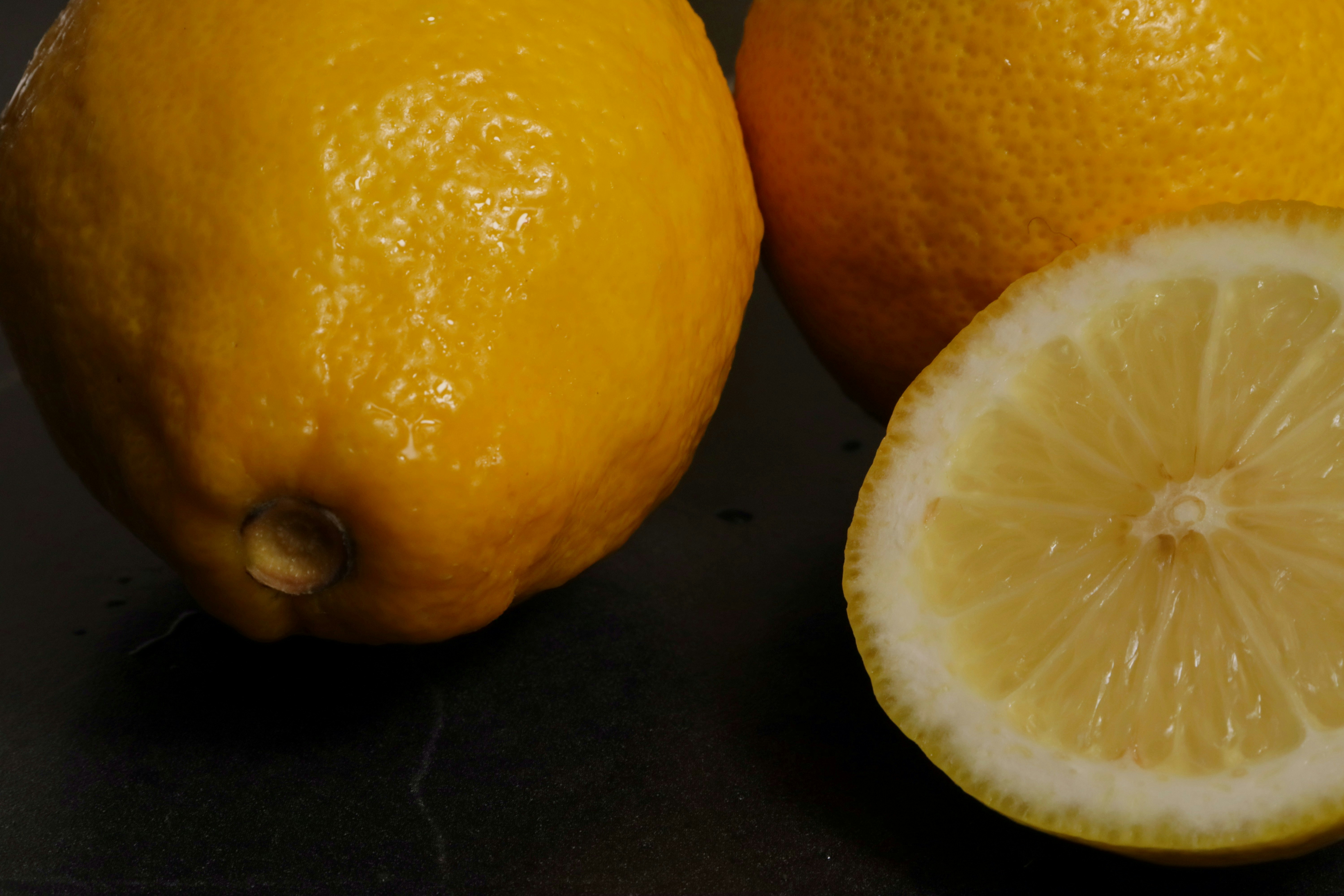 Two whole yellow lemons and one halved lemon on a dark surface