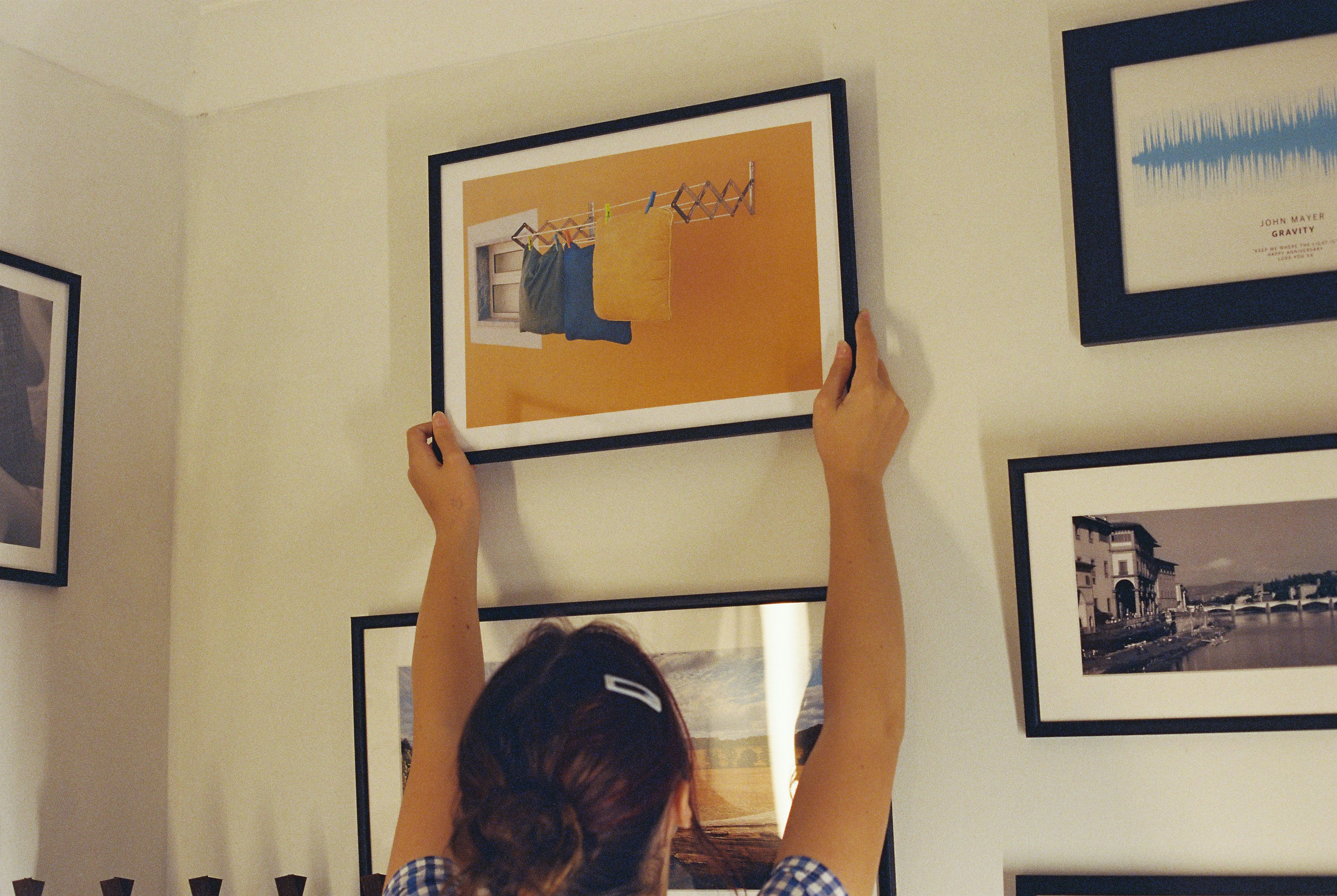 A person hanging framed pictures on a gallery wall