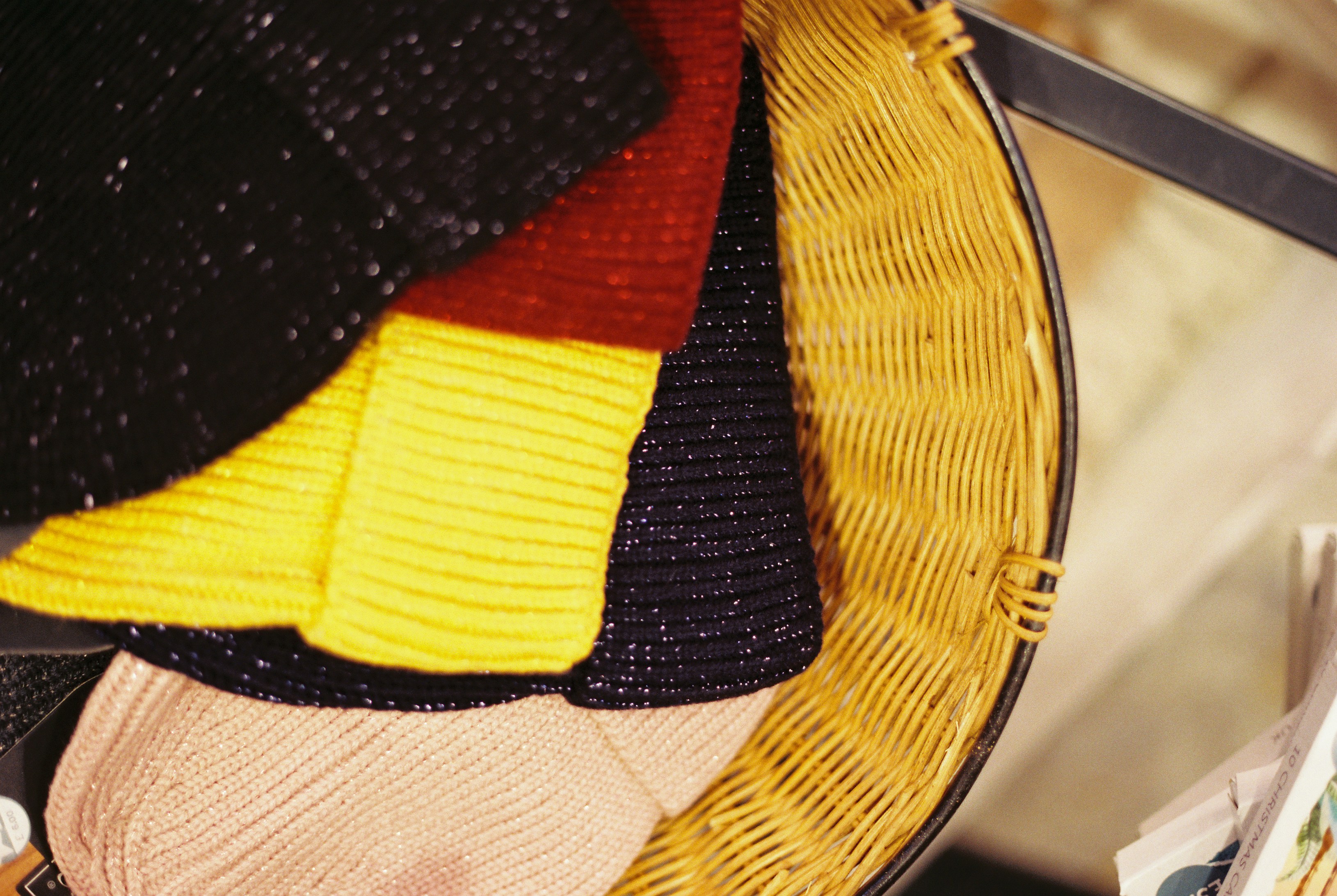 Colourful knitted hats folded together inside a woven wicker basket