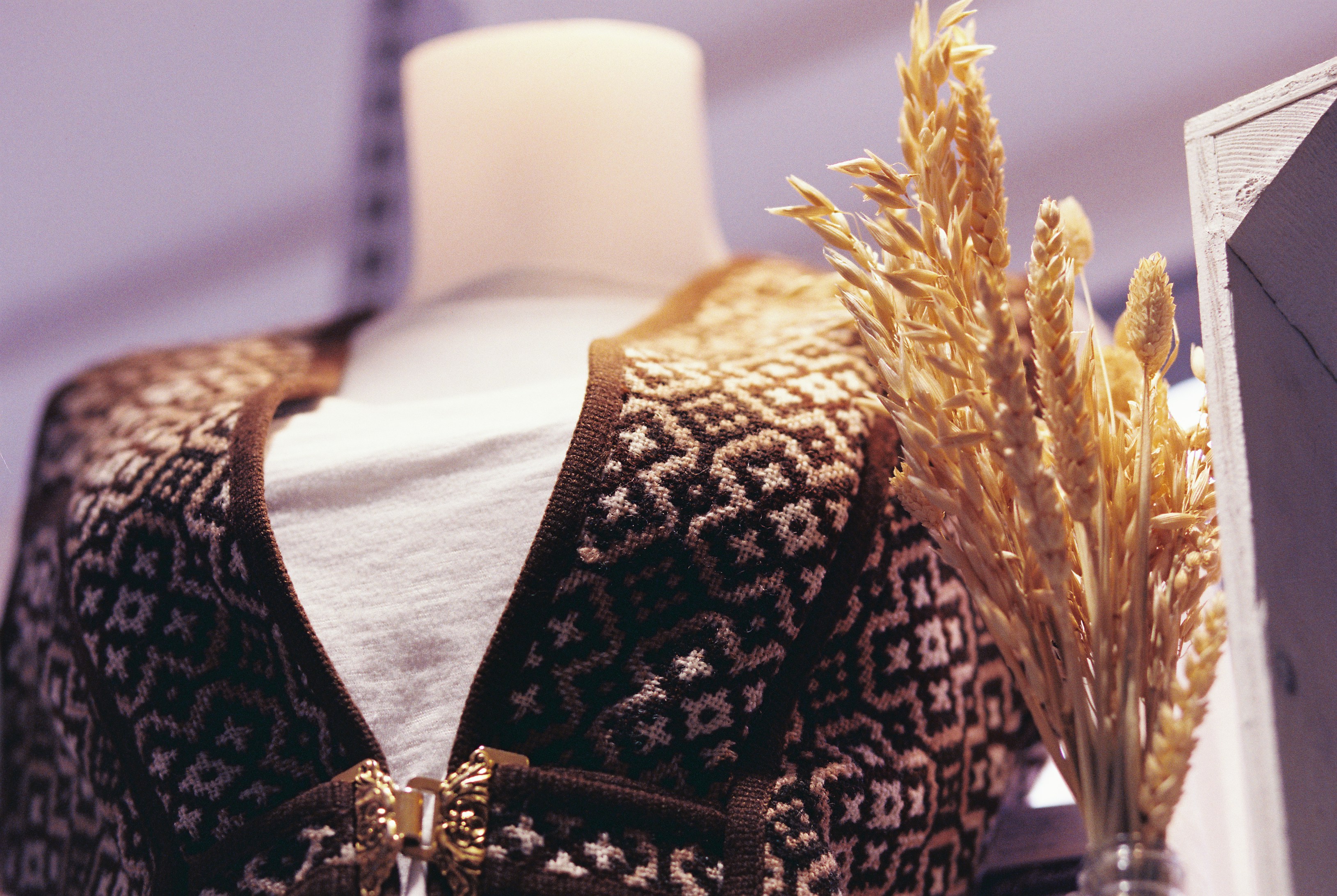 A patterned knit garment on a mannequin beside a bundle of dried wheat stems