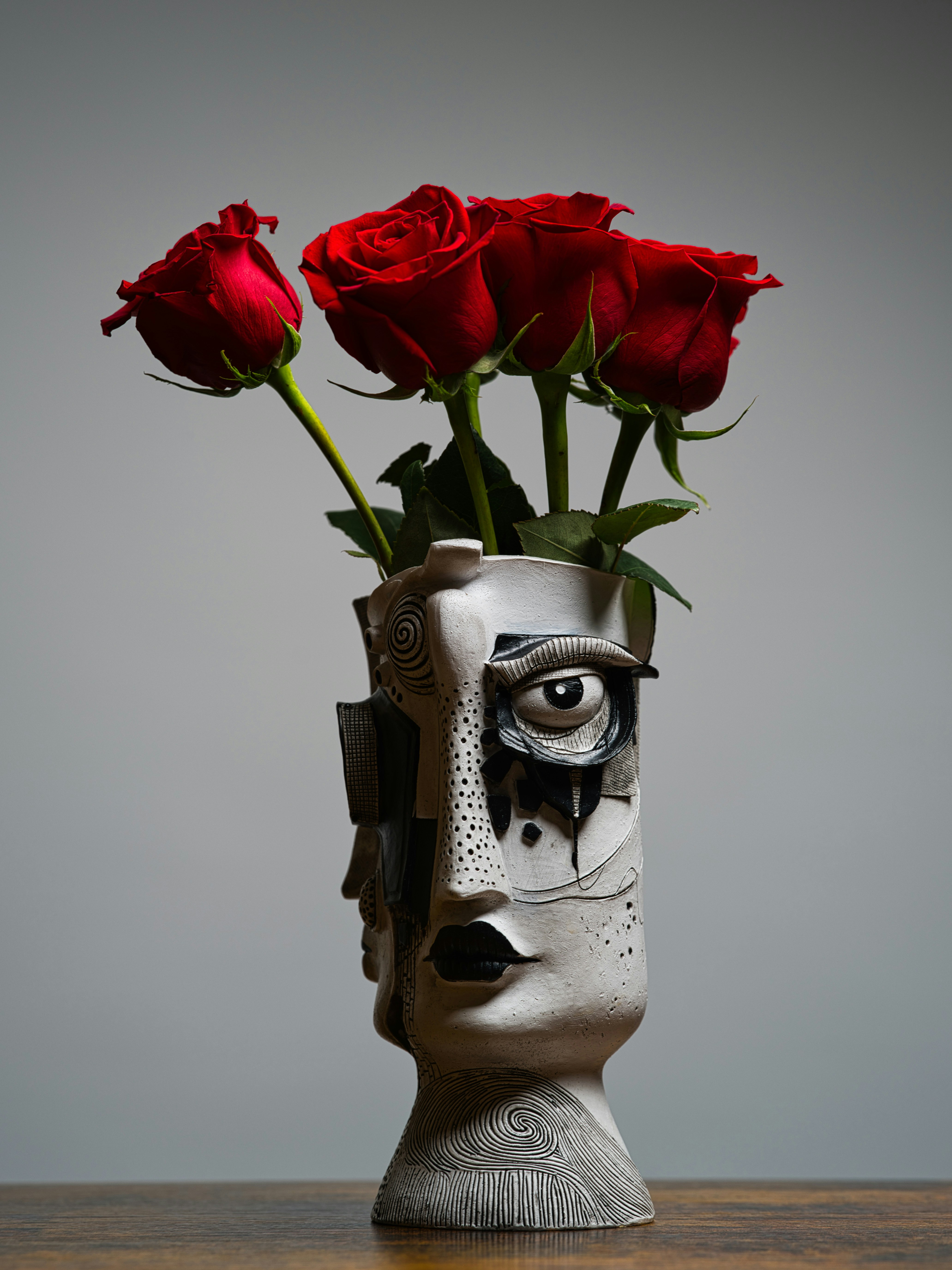 Cuatro rosas rojas en un jarrón de cerámica blanca con forma de rostro humano