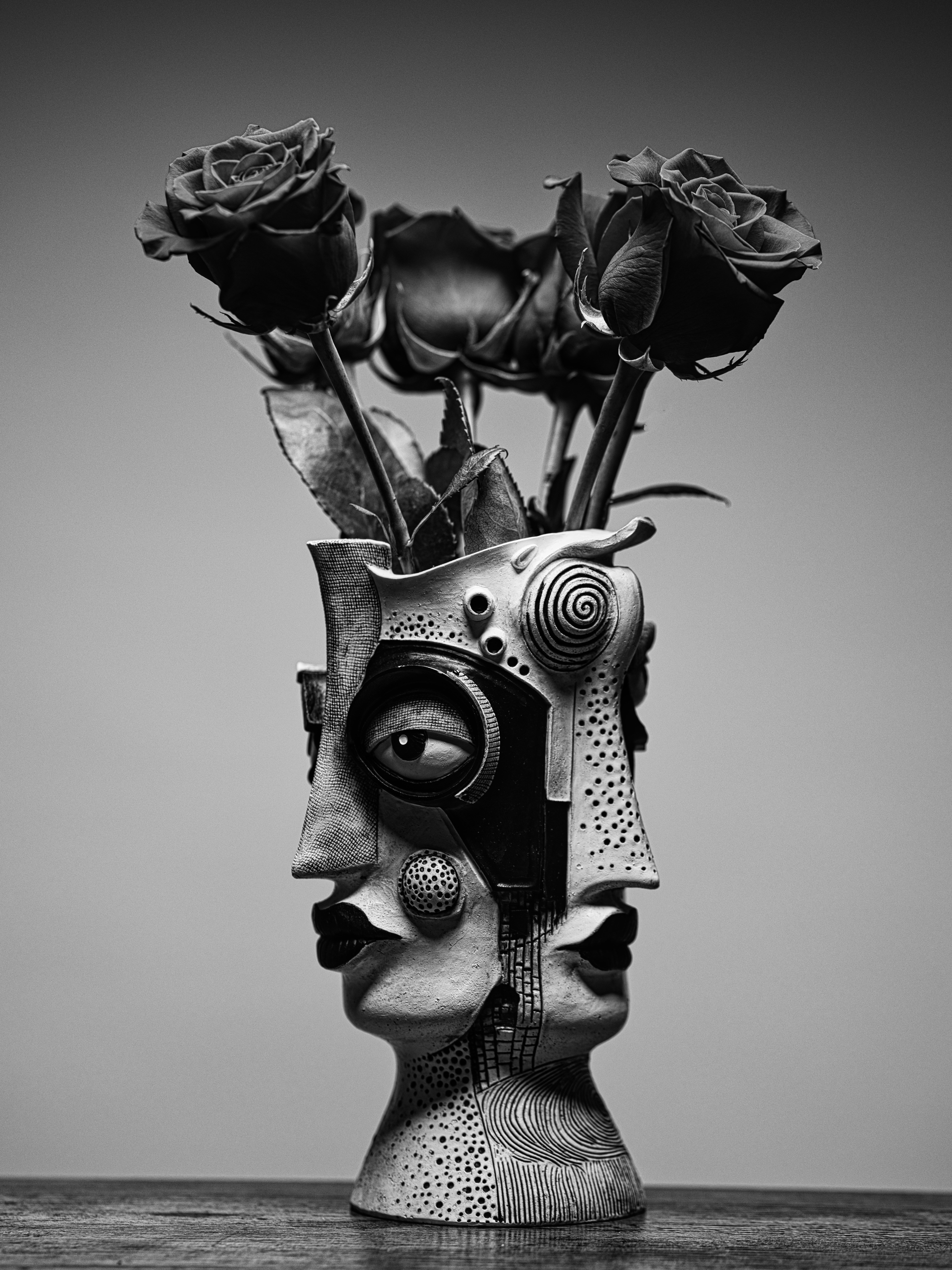 Un jarrón cerámico blanco y negro con forma de rostro que sostiene tres rosas