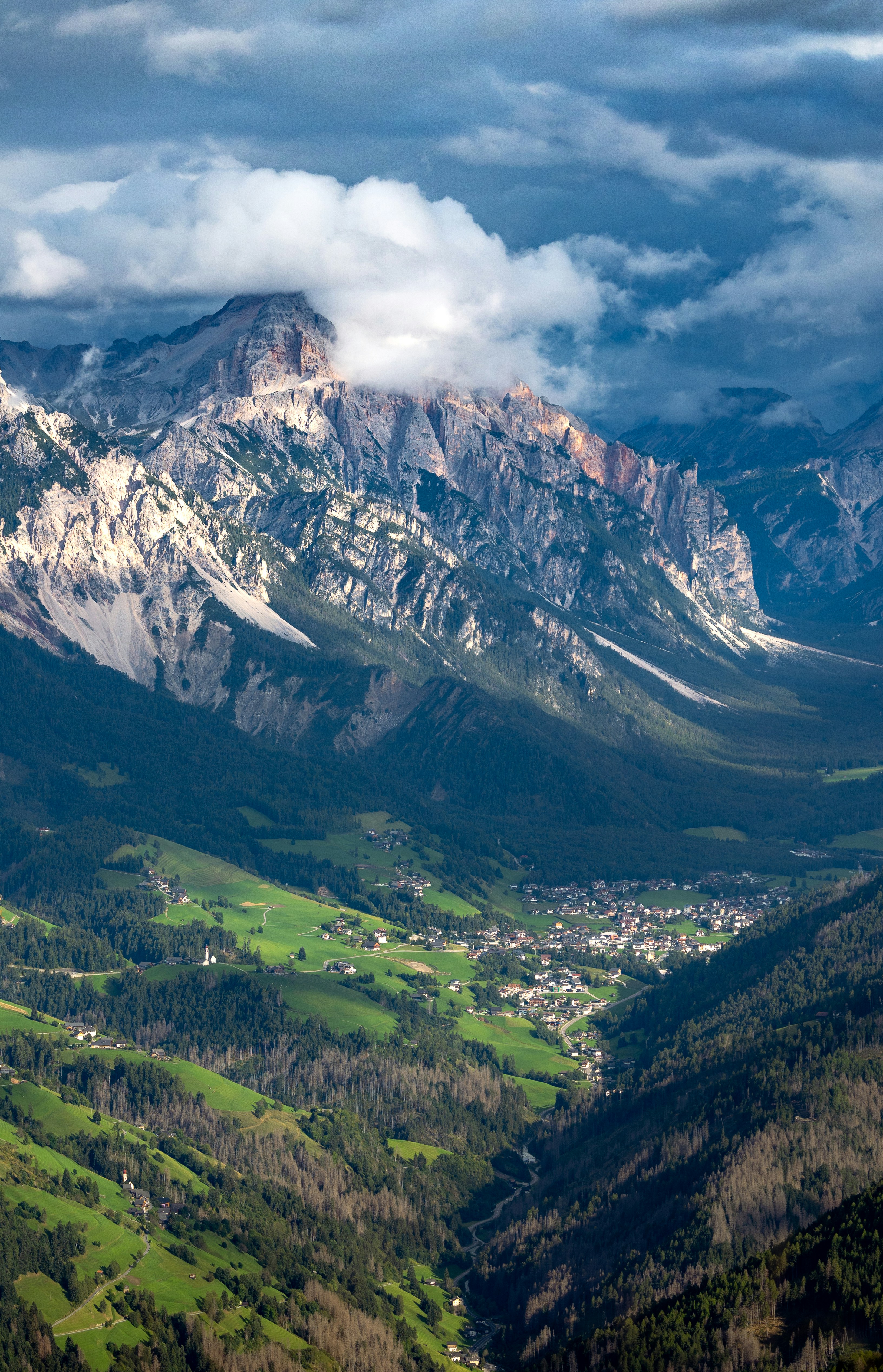 A small village nestled in a green valley beneath towering jagged mountain peaks