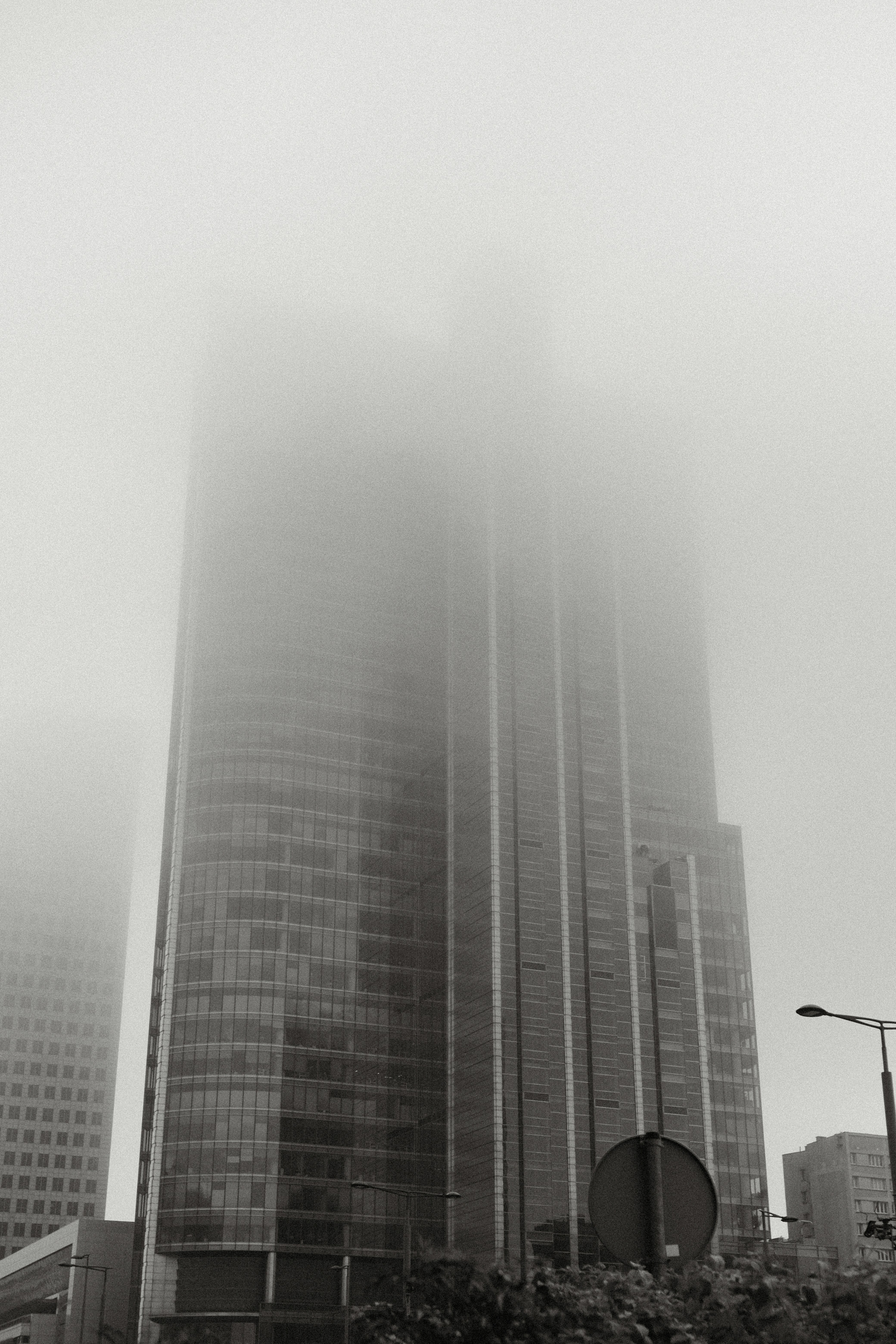 A modern glass skyscraper partially obscured by thick grey fog in a city