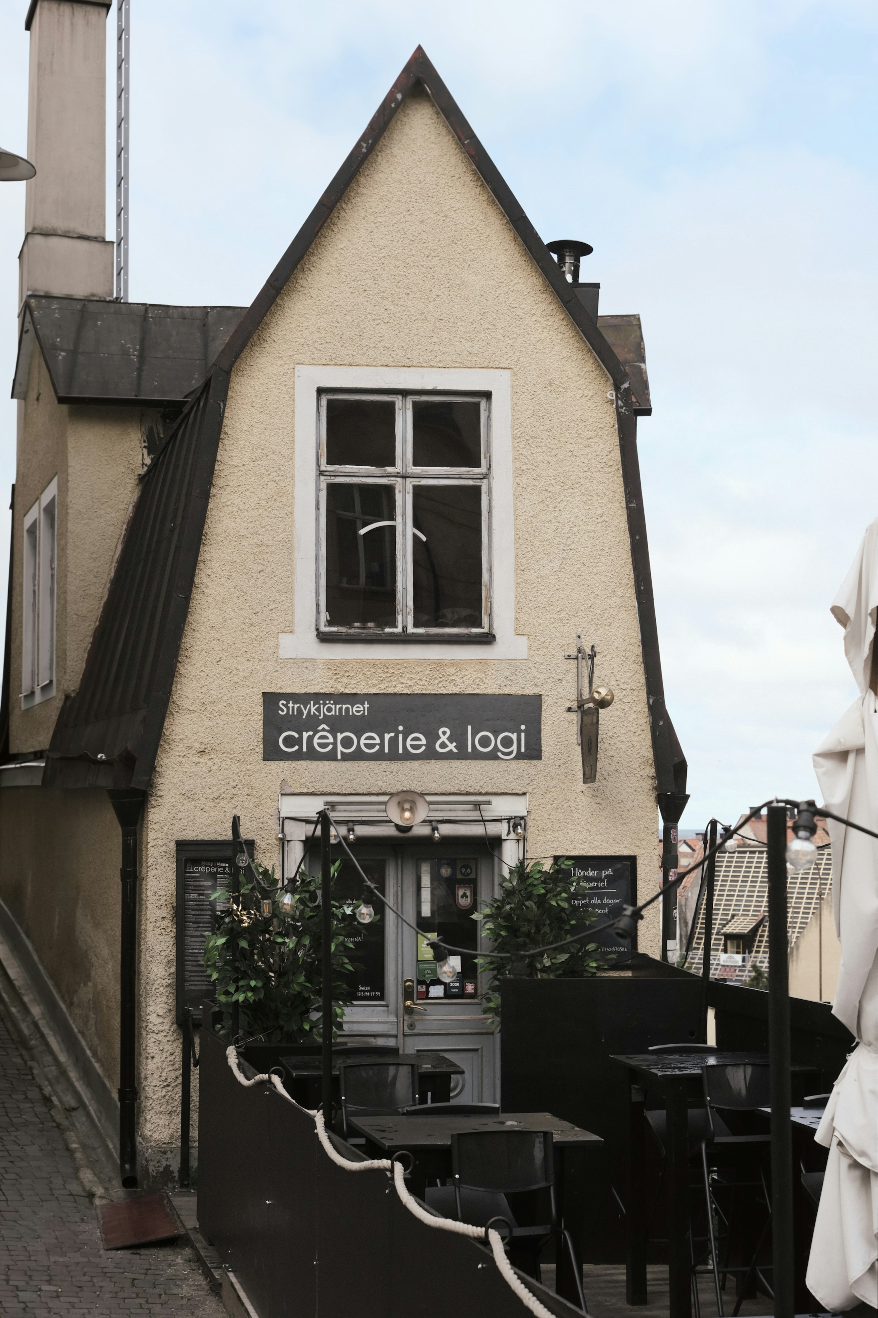 Un bâtiment étroit jaune avec un panneau indiquant crêperie & logi au-dessus d’une terrasse