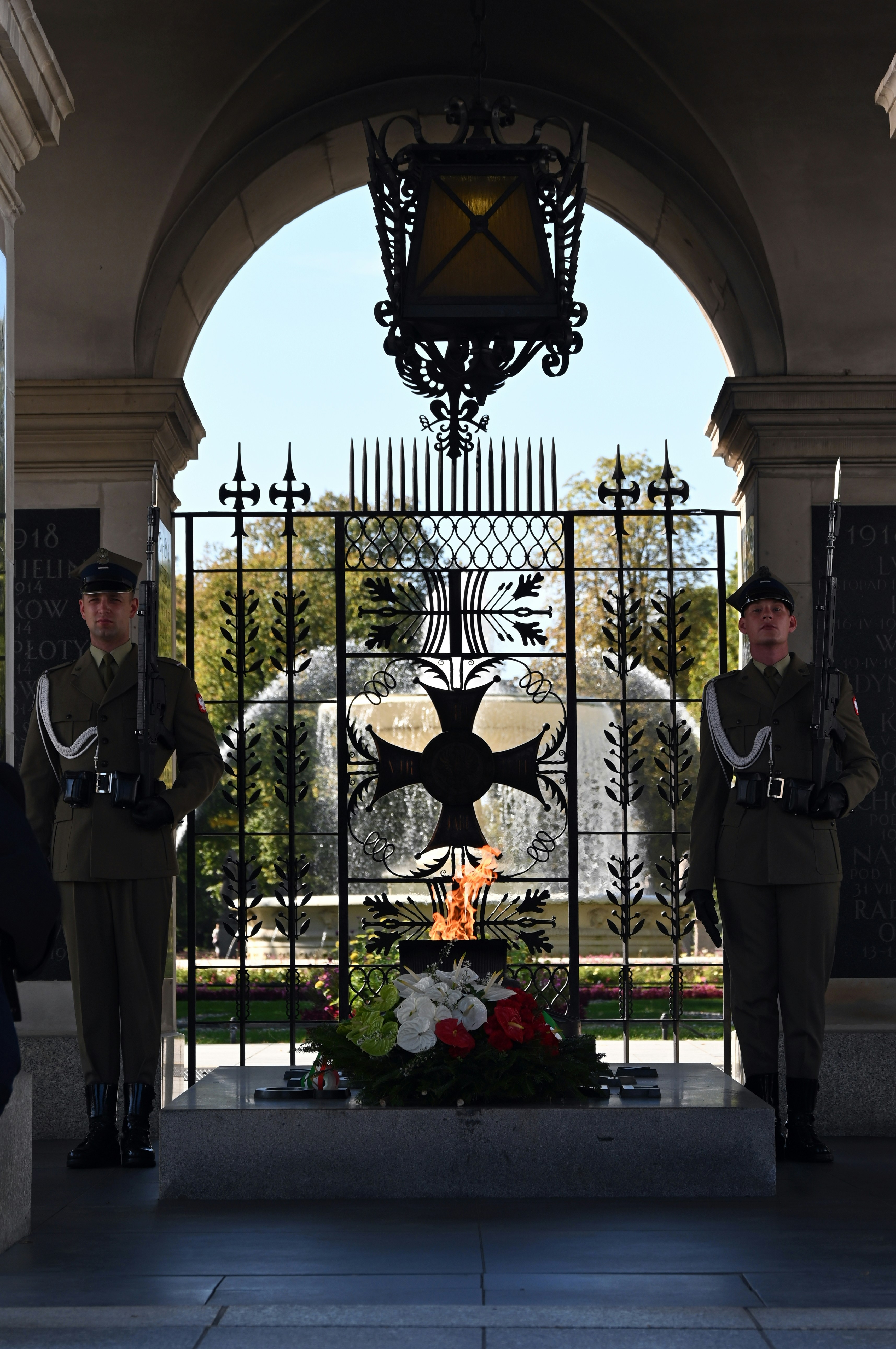 Two guards in uniform flanking an eternal flame at a memorial arch