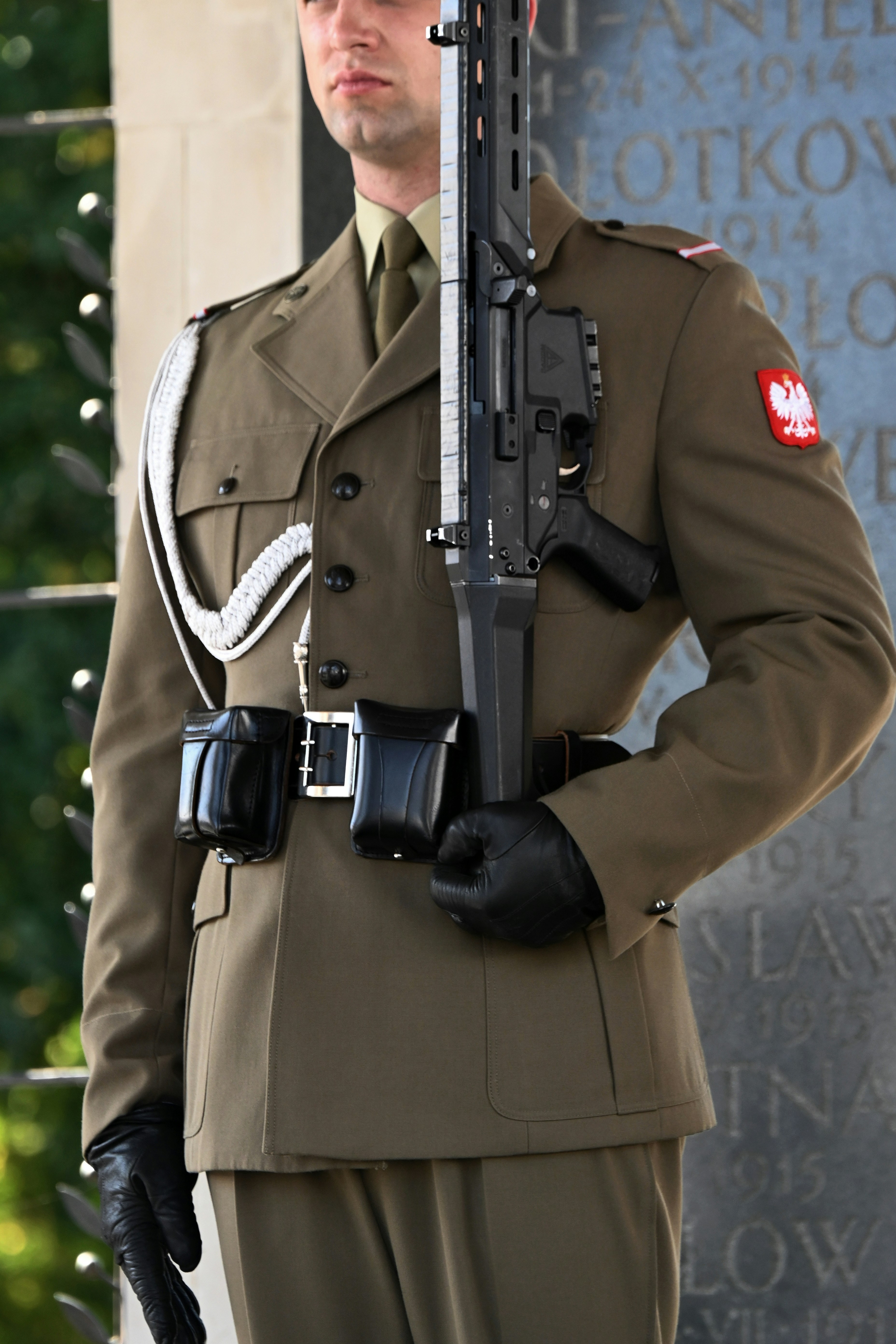 A soldier in olive uniform holding a rifle in front of a stone monument