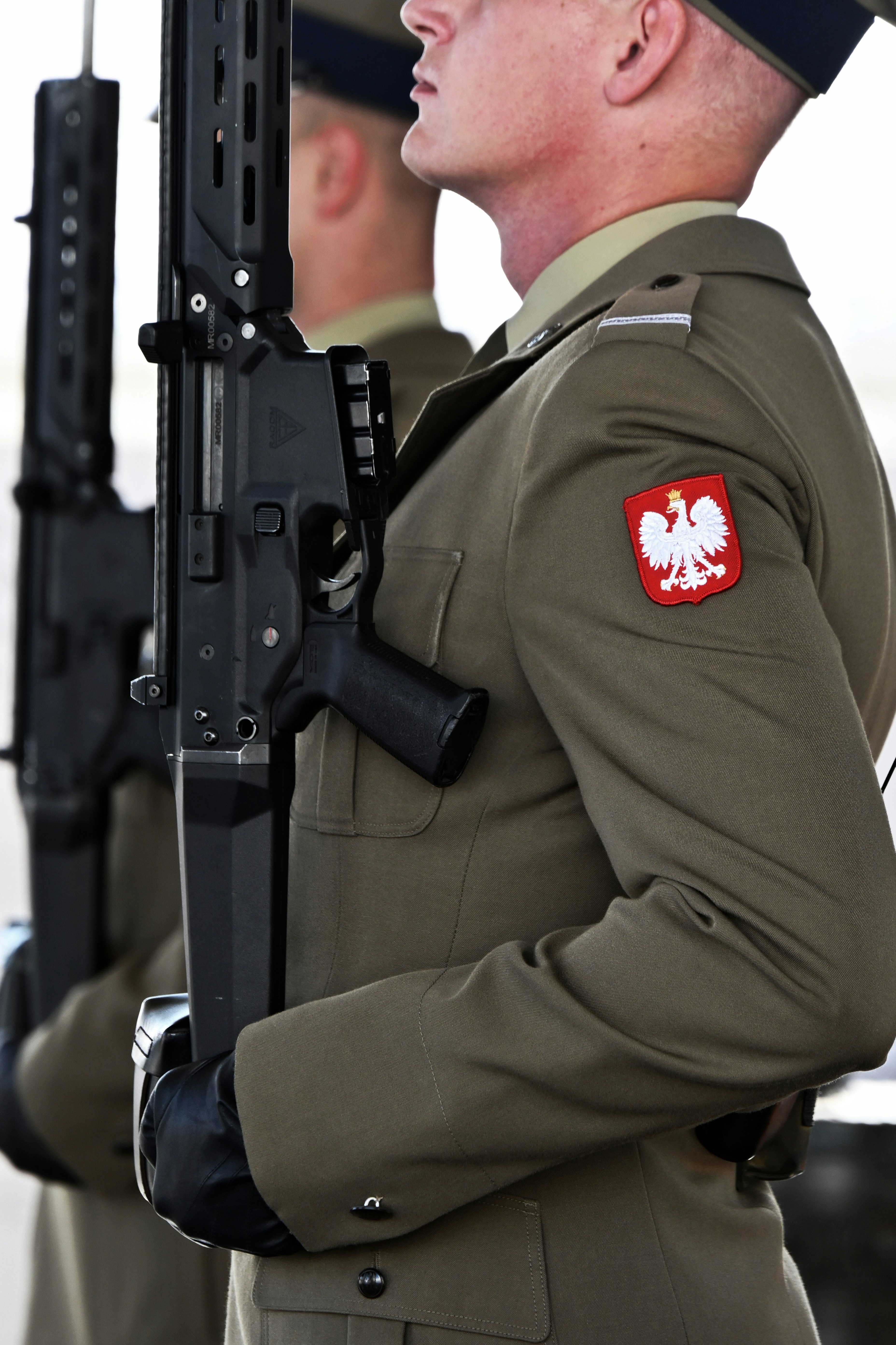 A soldier in olive uniform with a Polish eagle patch holding a rifle