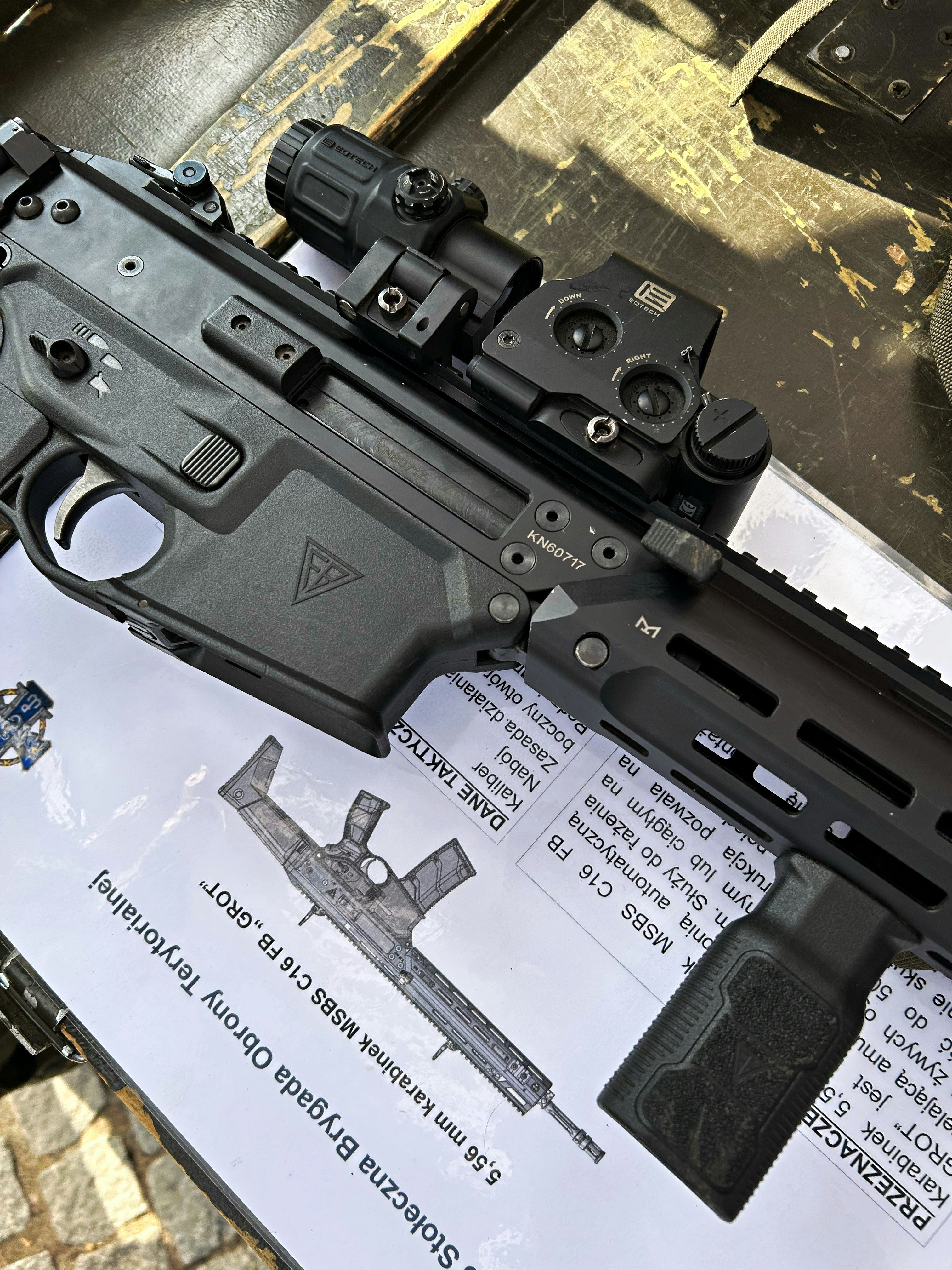 A black assault rifle with an optical sight resting on a technical manual