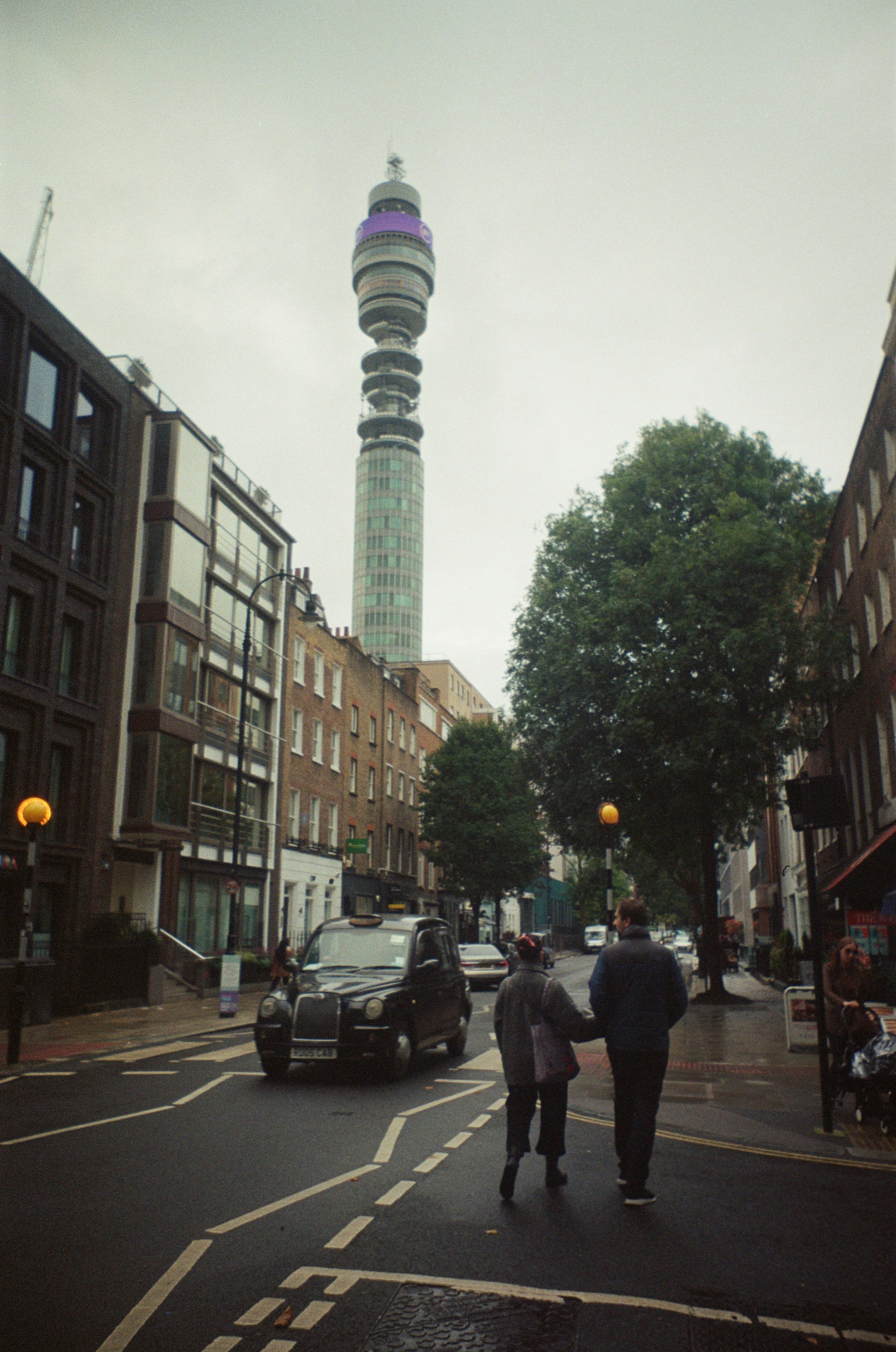Two people walking on a street in London toward the BT Tower