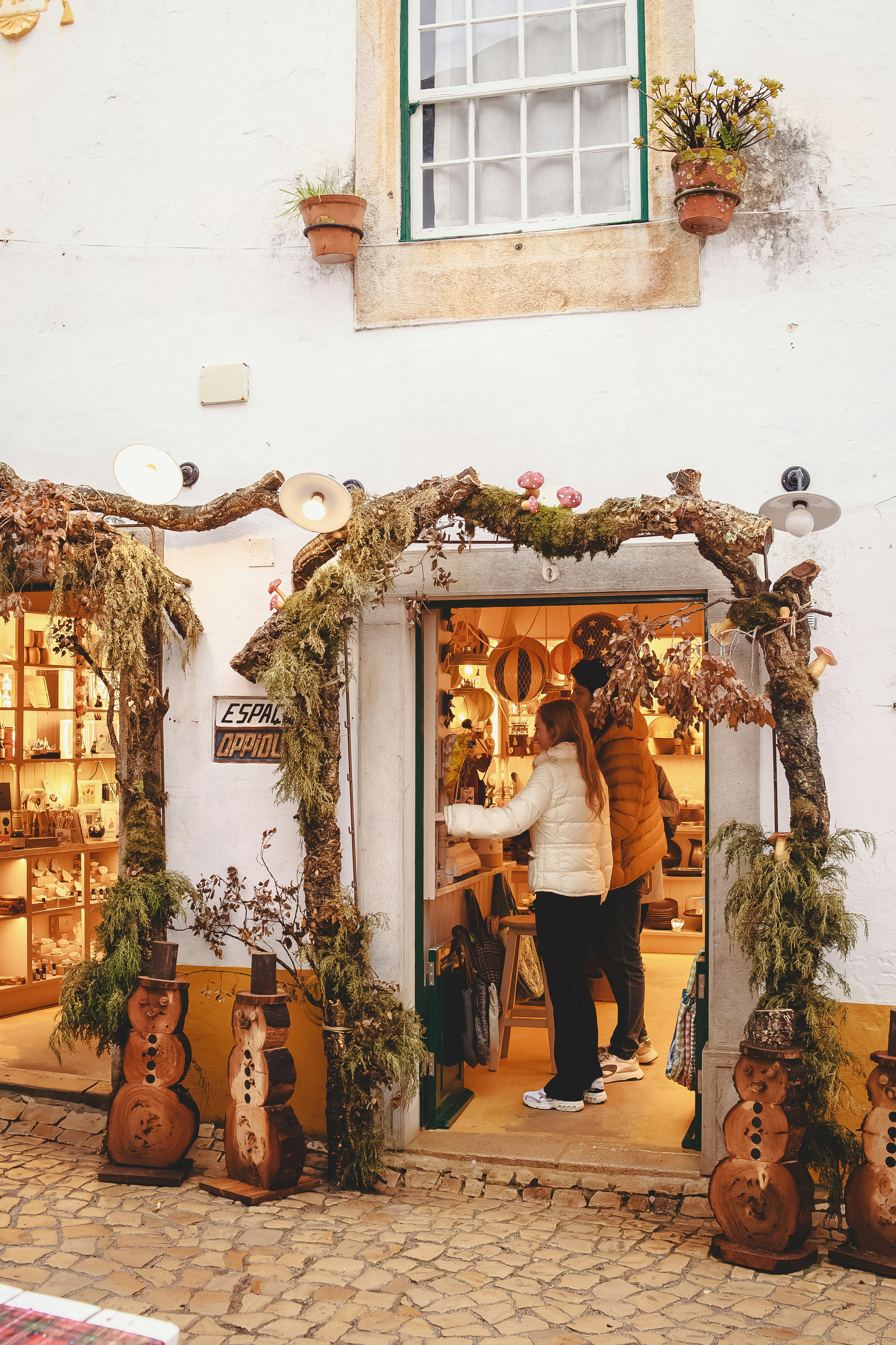 Two people browsing inside a shop entrance decorated with mossy branches and wooden snowmen