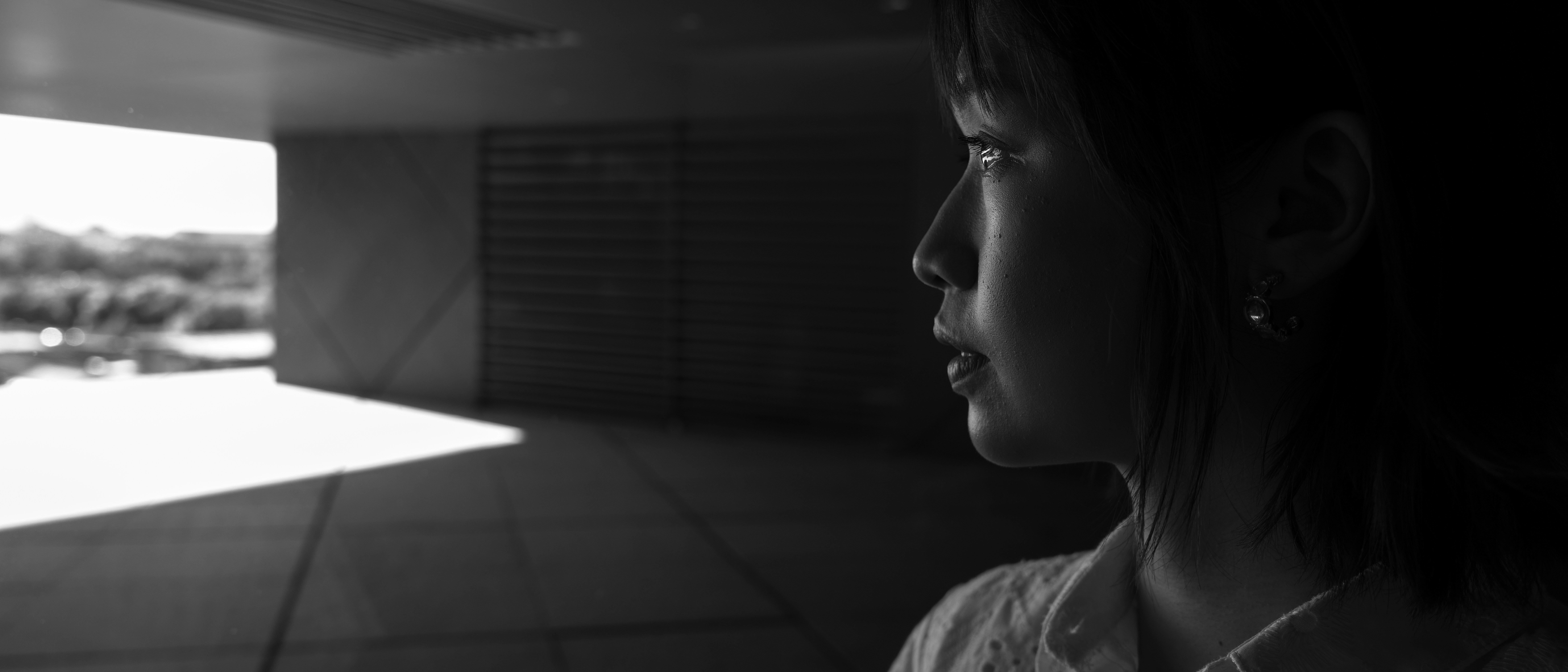 A woman in profile looking toward a bright doorway in black and white