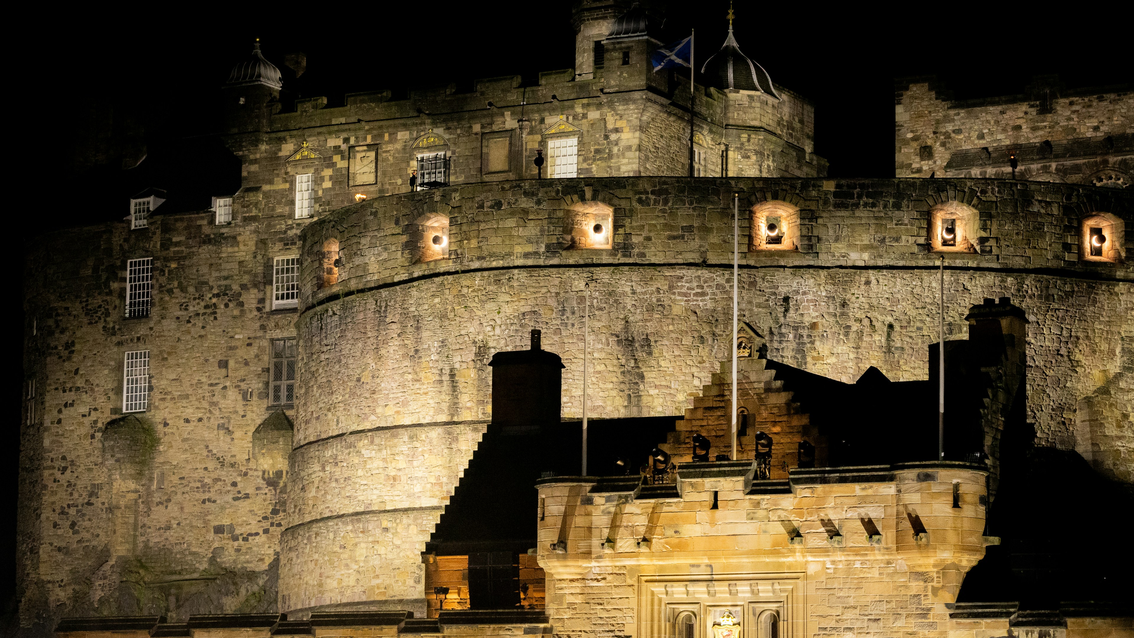 Edinburgh Castle illuminated at night with stone walls and a Scottish flag