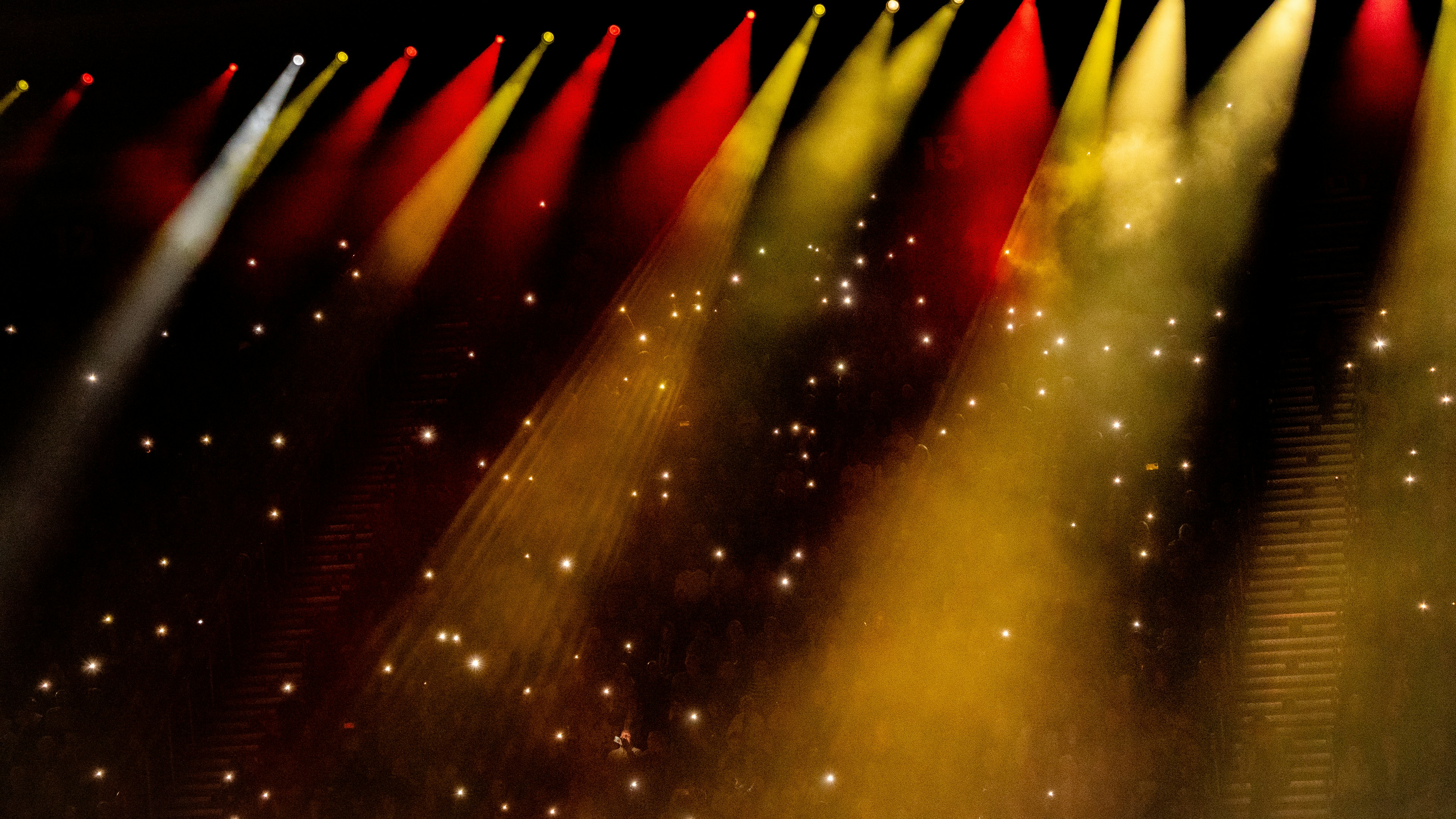 Red and yellow stage lights shining over a crowd holding glowing mobile phones