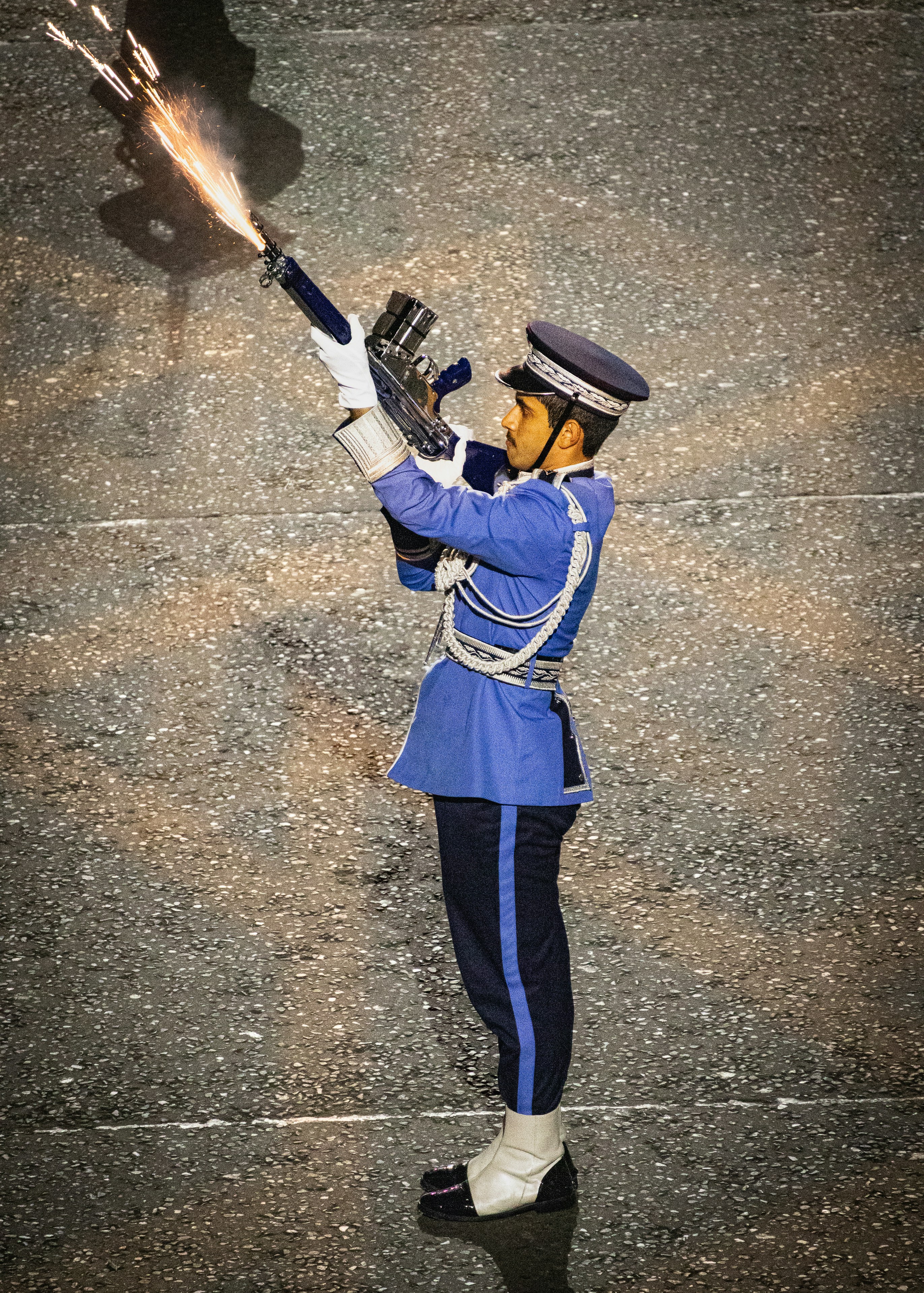 A guard in a blue uniform firing a rifle with sparks on a street