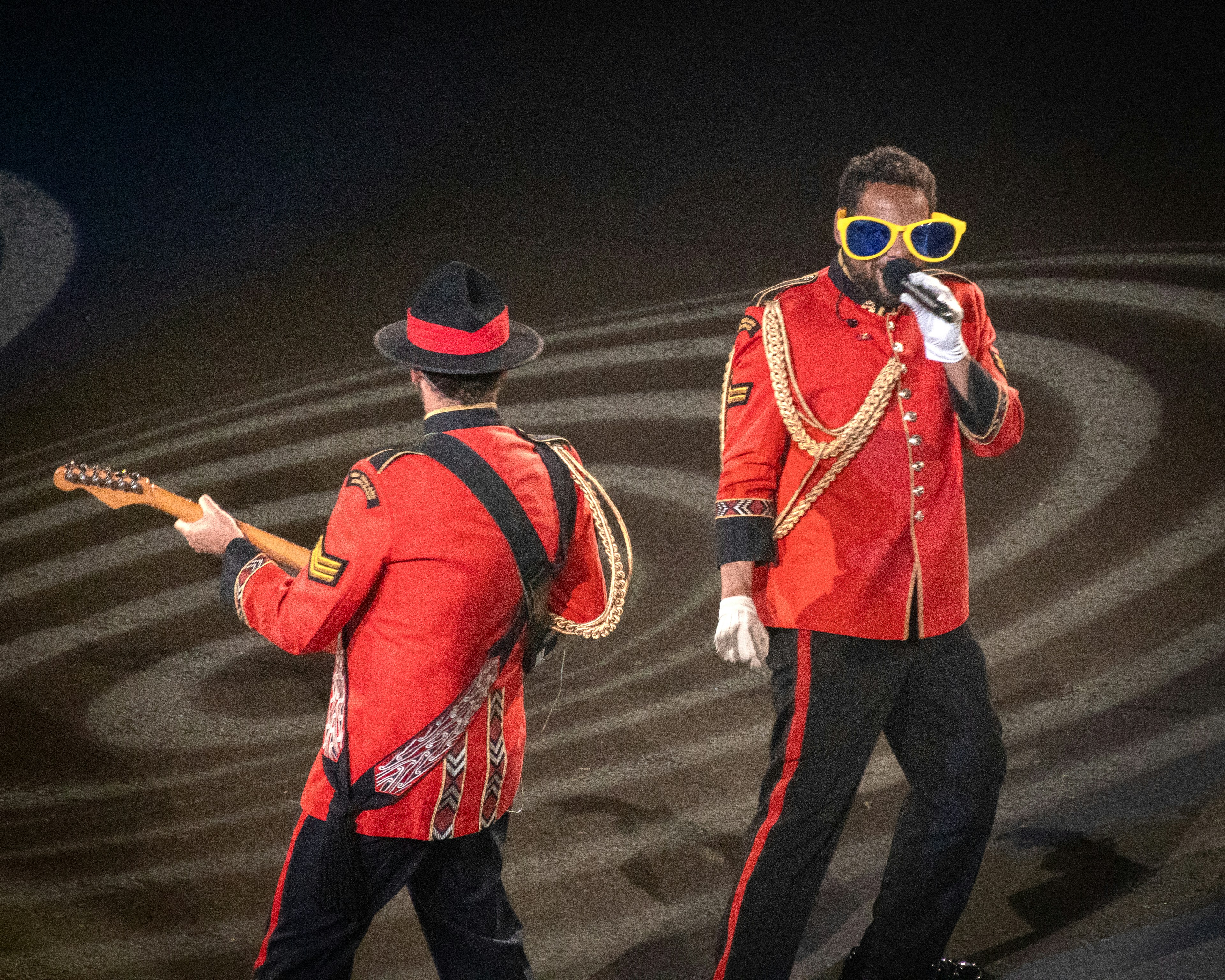 A person playing guitar and a person singing in red military-style jackets