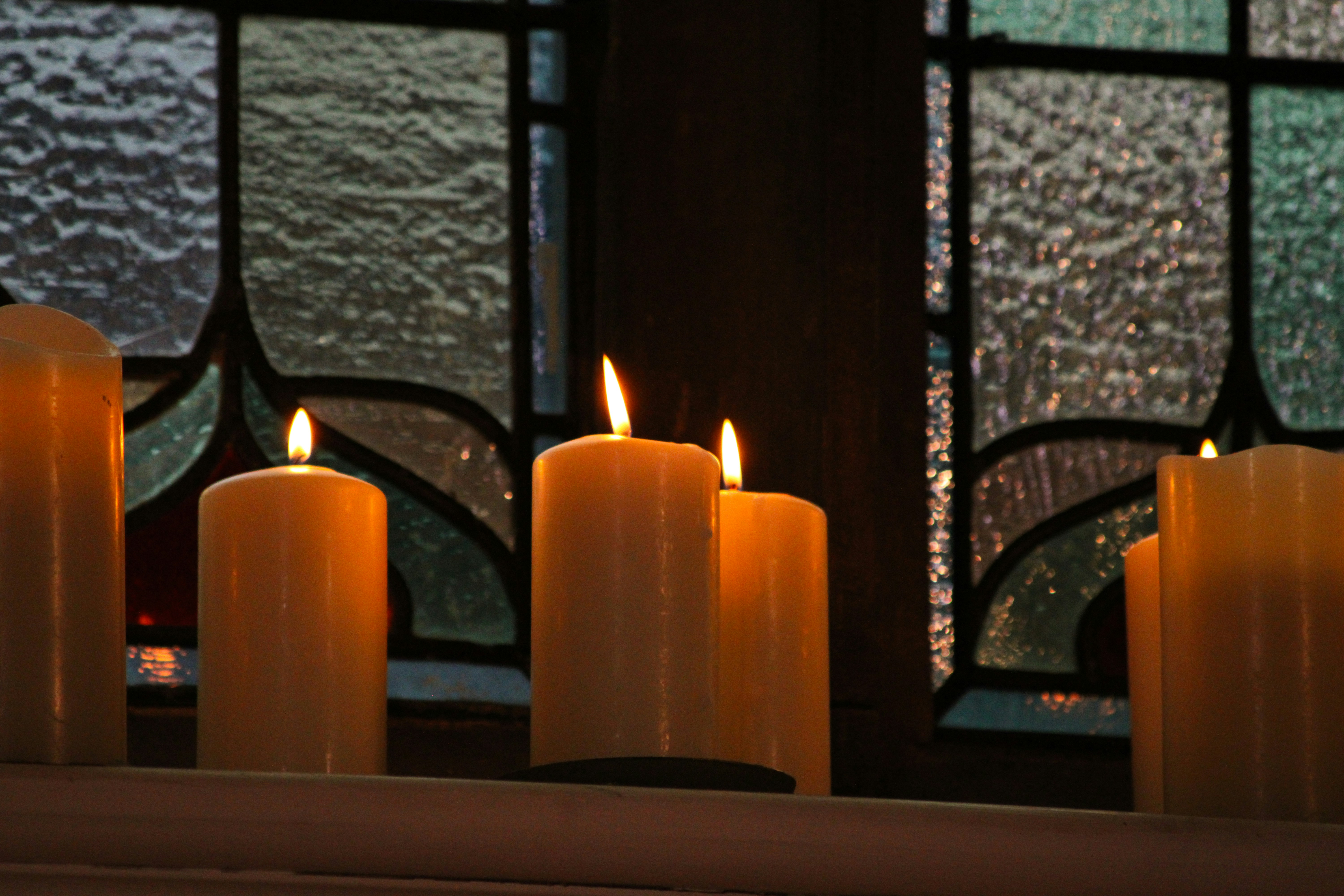 Lit pillar candles on a ledge in front of a textured glass window