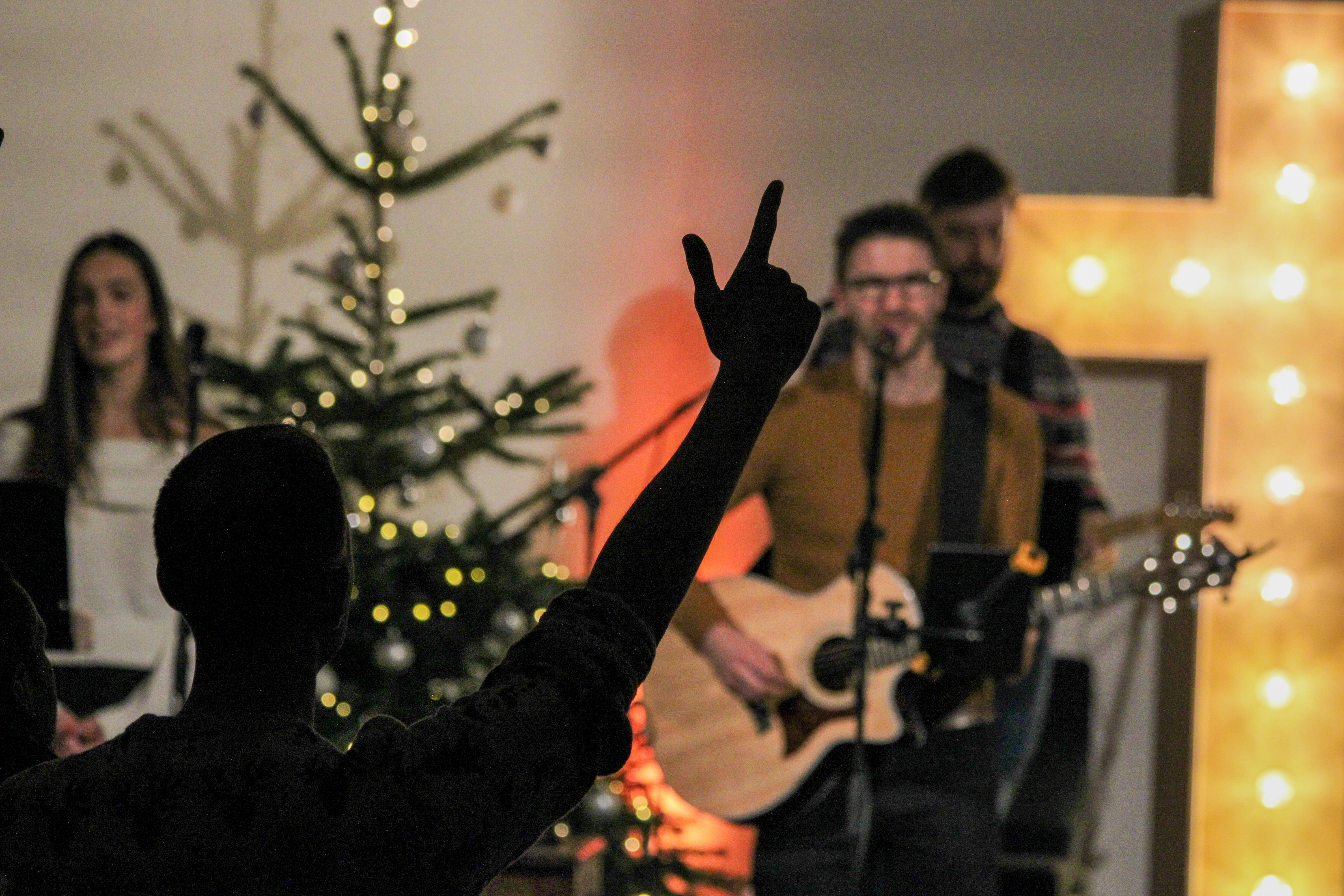 A person with a raised hand before a band and a lit Christmas tree