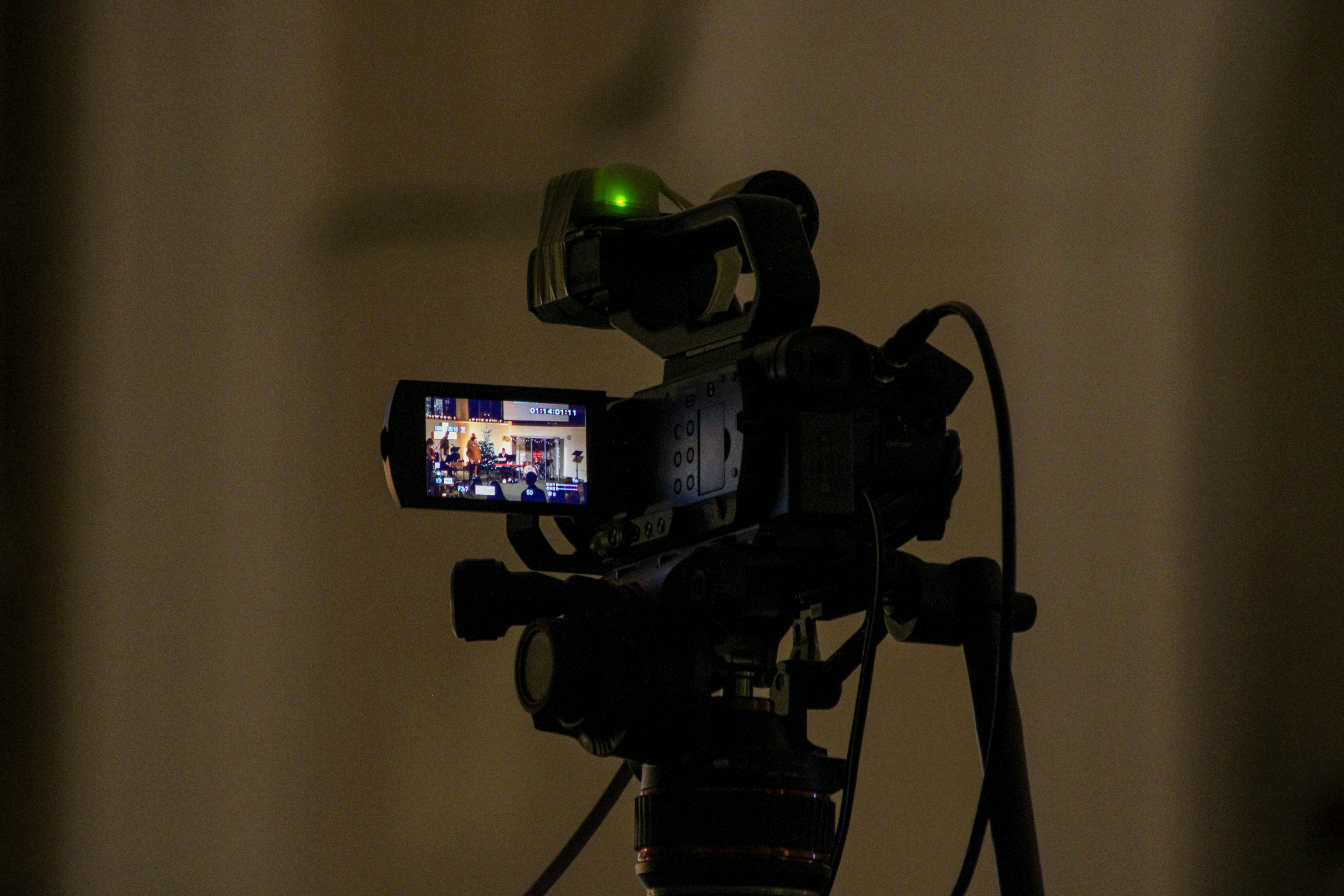 A professional video camera on a tripod with a glowing green tally light