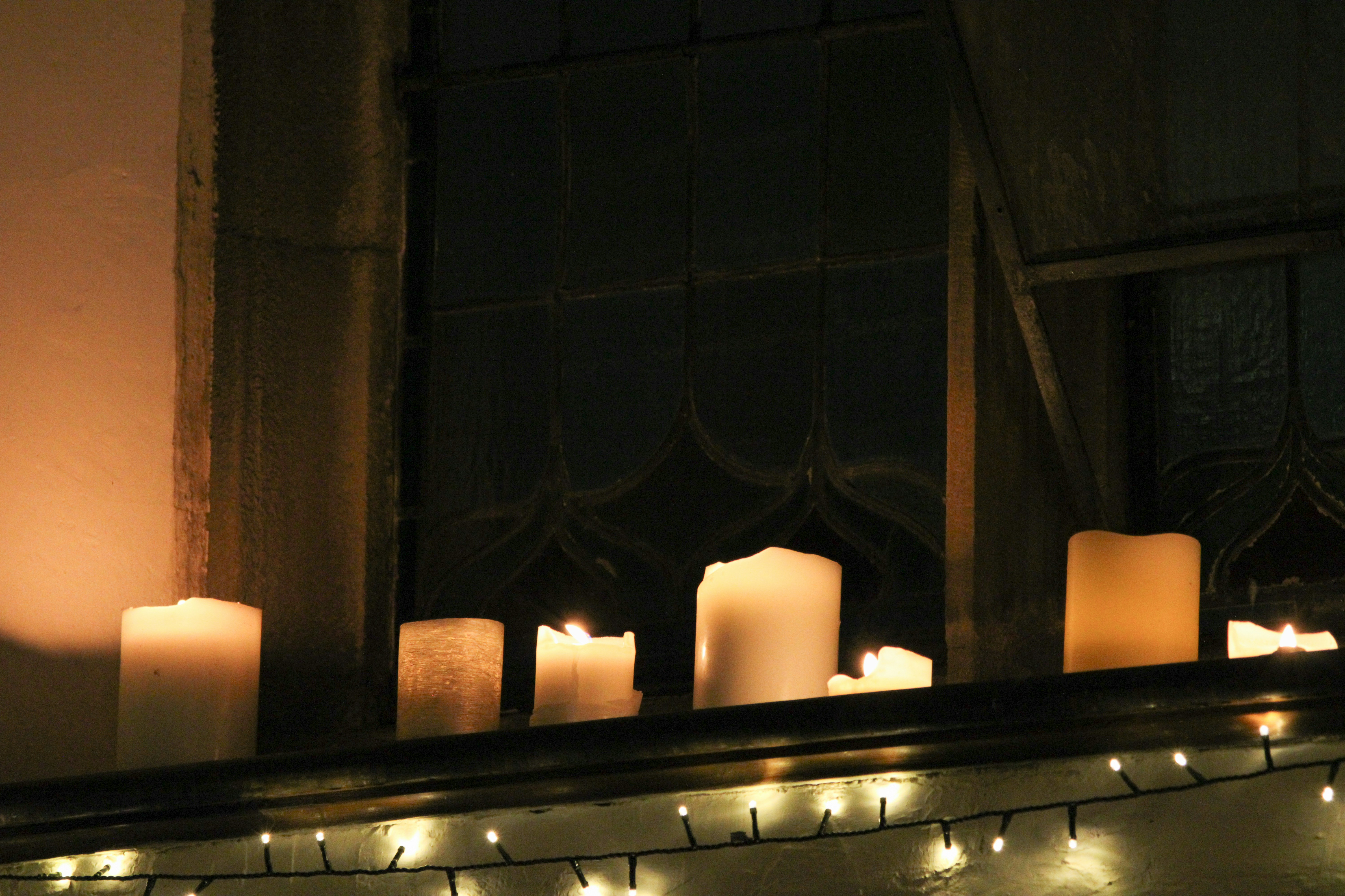 White candles glowing on a dark windowsill in front of a leaded glass window