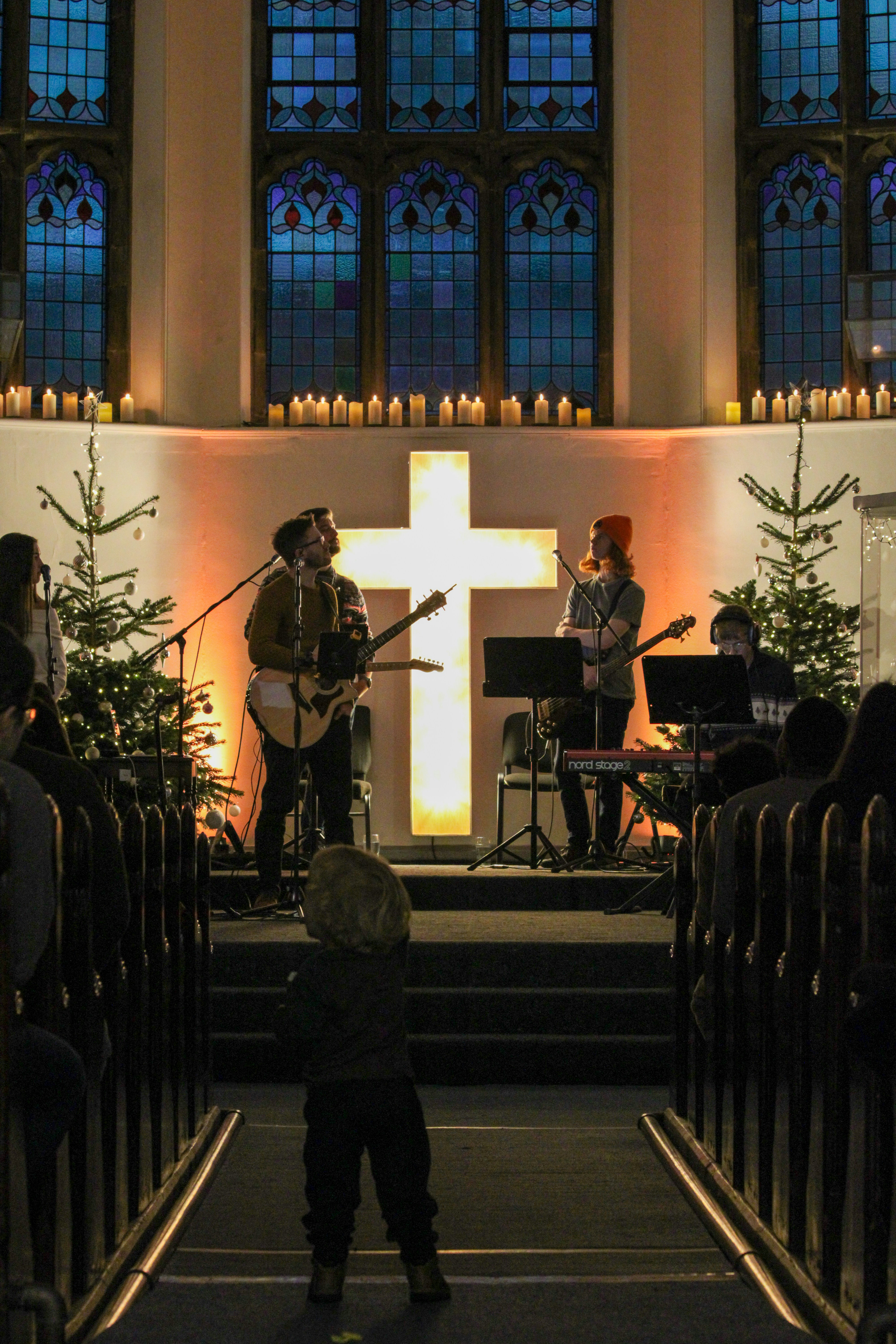 A band performing on a church stage with a glowing cross and Christmas trees