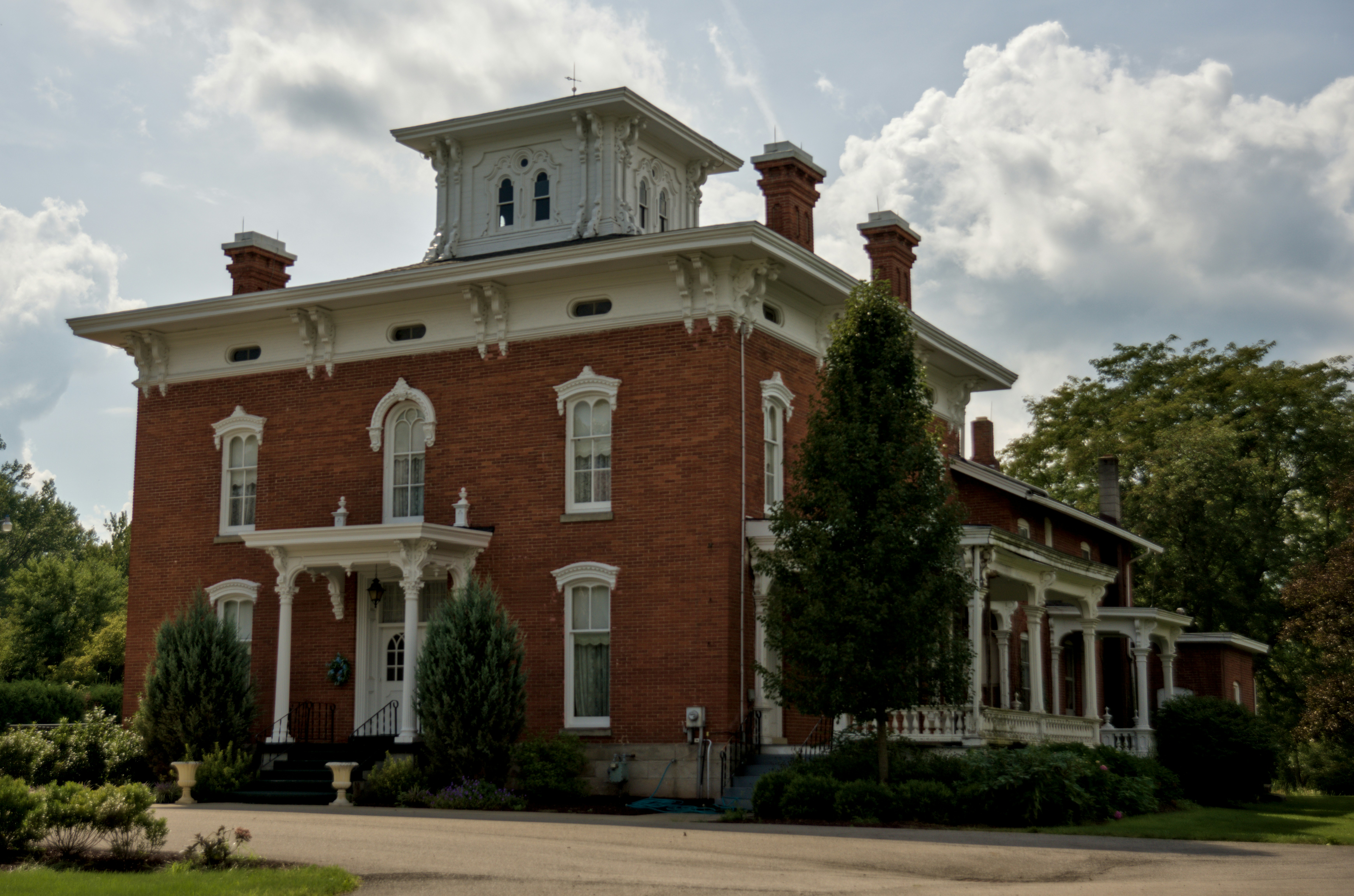 A historic red brick Italianate house with a white cupola and wrap-around porch