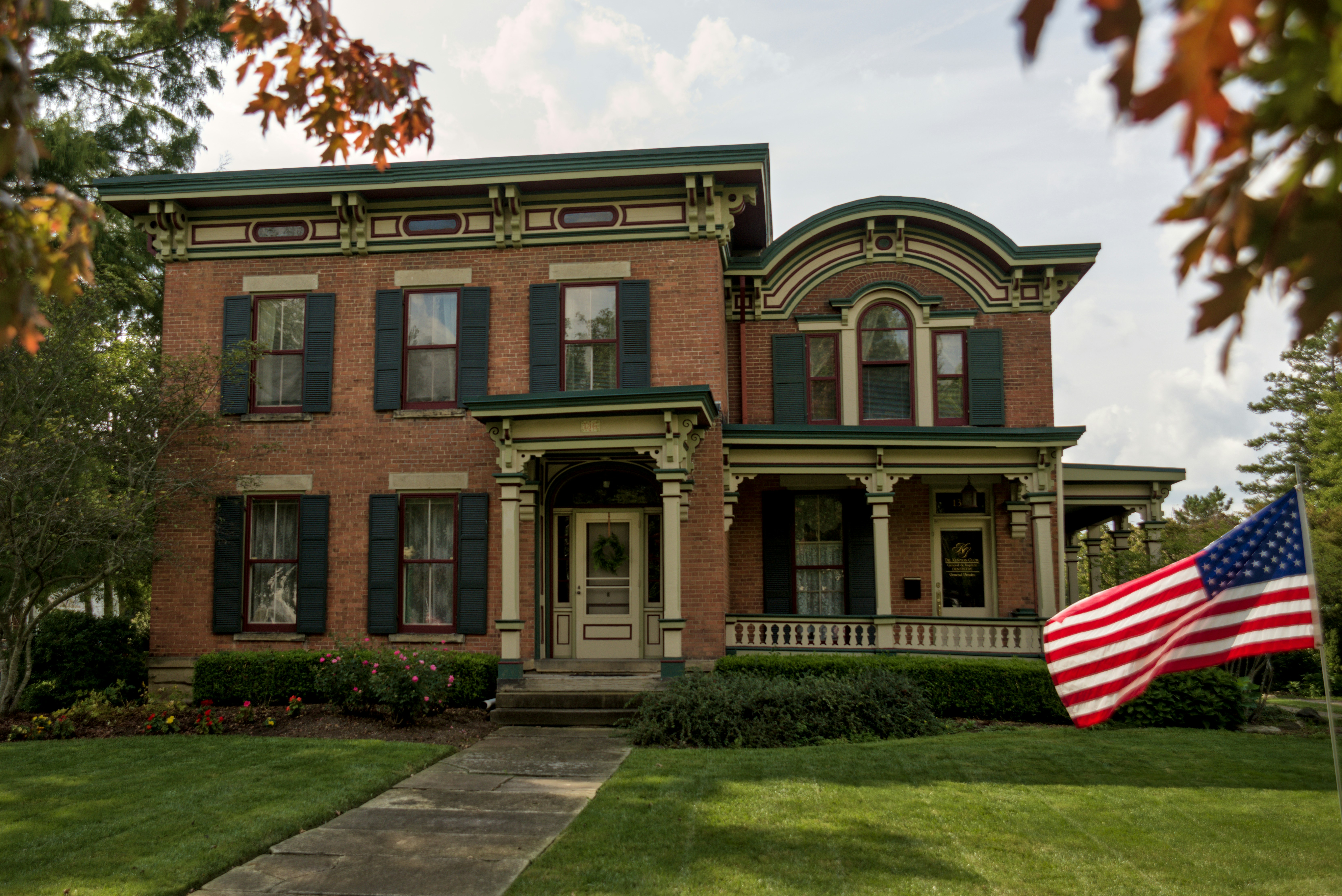 A historic brick house with green shutters and an American flag on the lawn