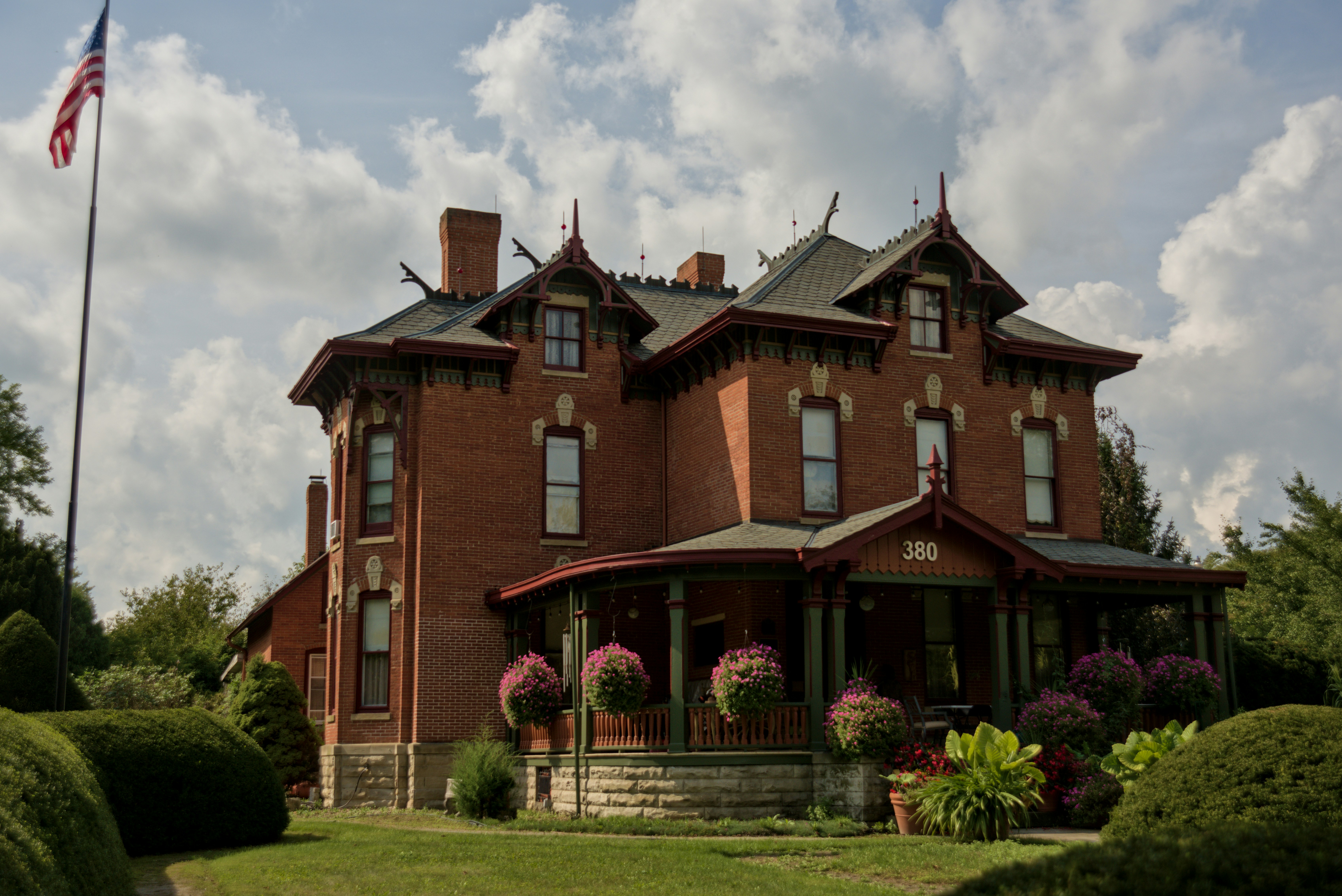 A red brick Victorian house with a porch and hanging flower baskets