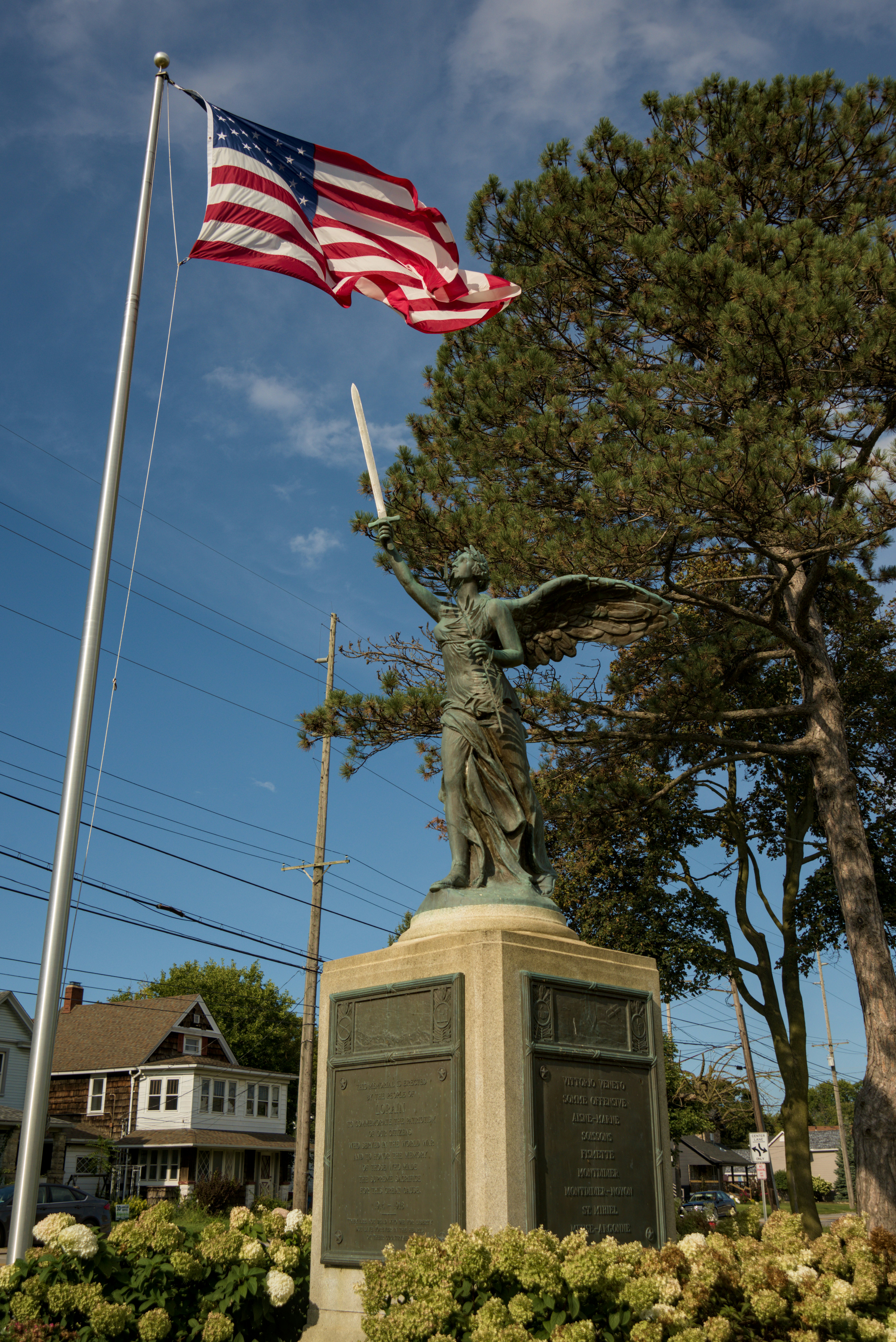 A bronze winged statue holding a sword near a waving American flag