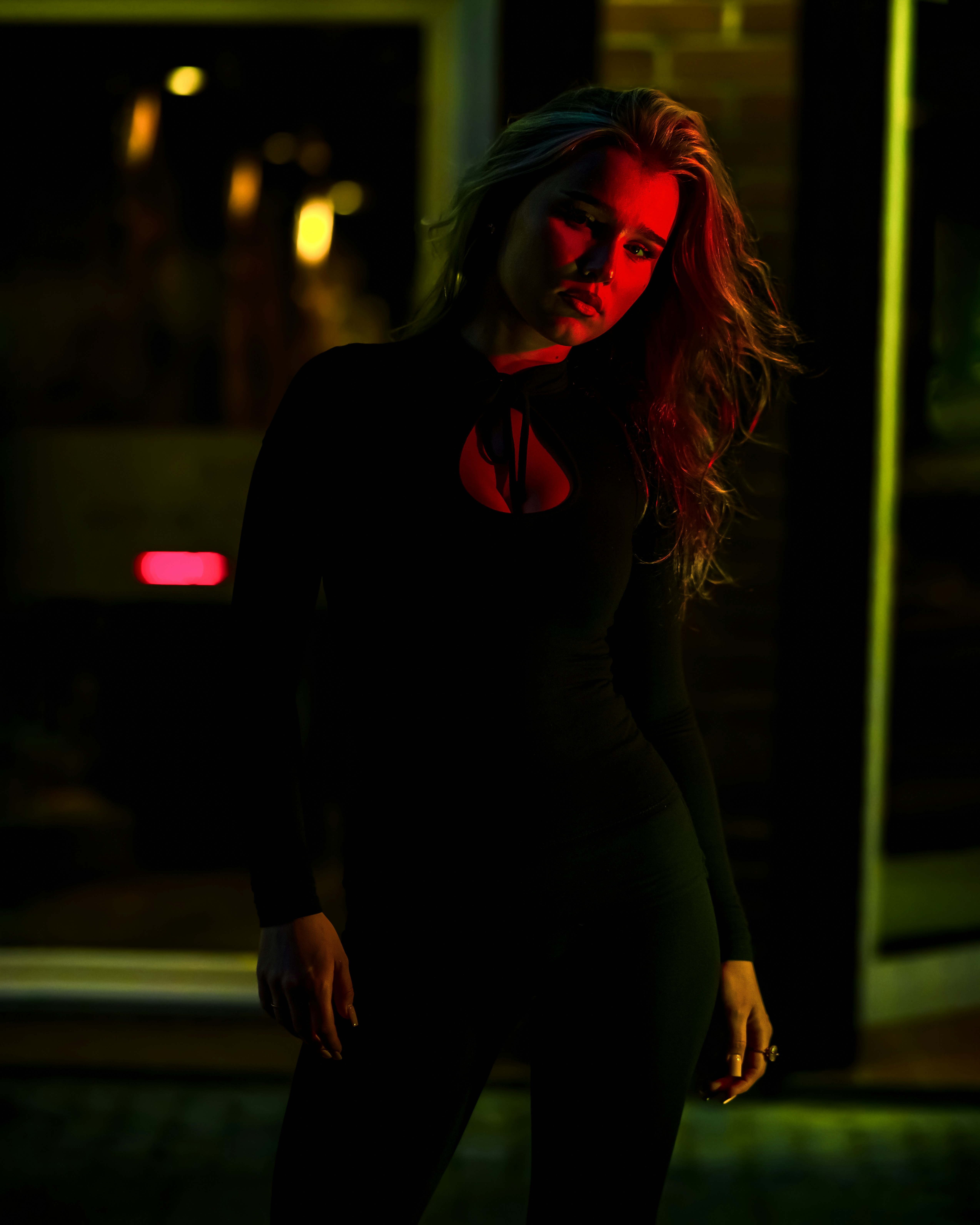 A woman in a black long-sleeved top illuminated by red and green neon light