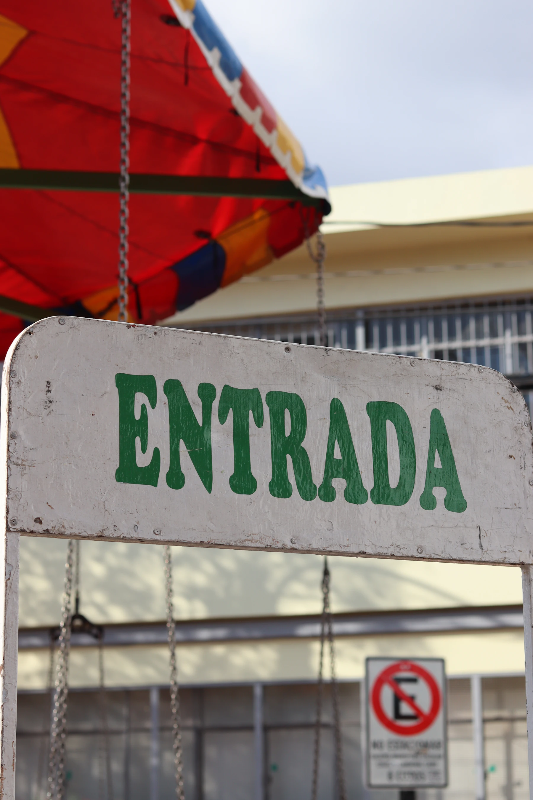 A white hand-painted sign reading ENTRADA in green capitals, with a red fairground canopy behind it