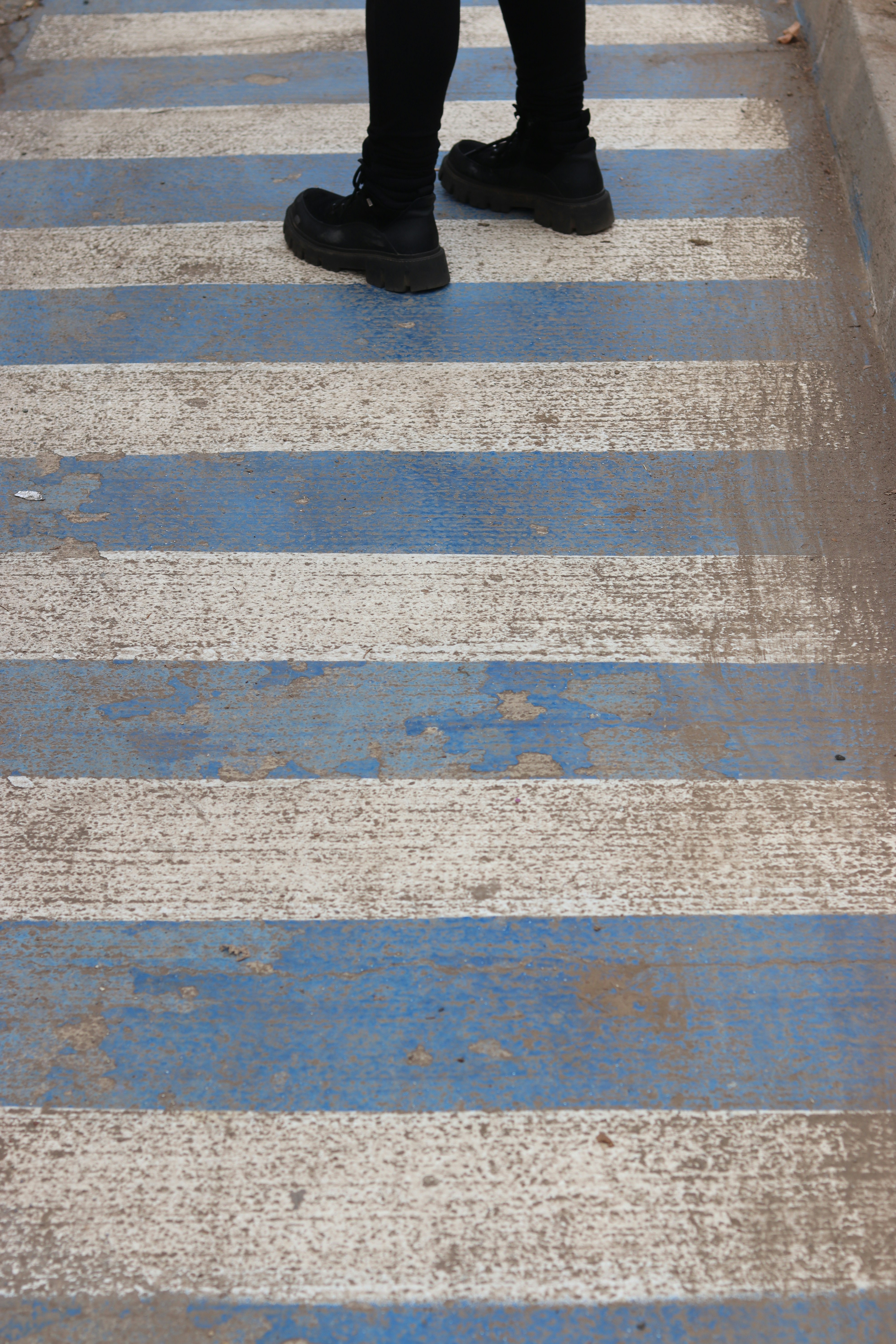 A person in black pants and boots standing on a blue and white crosswalk
