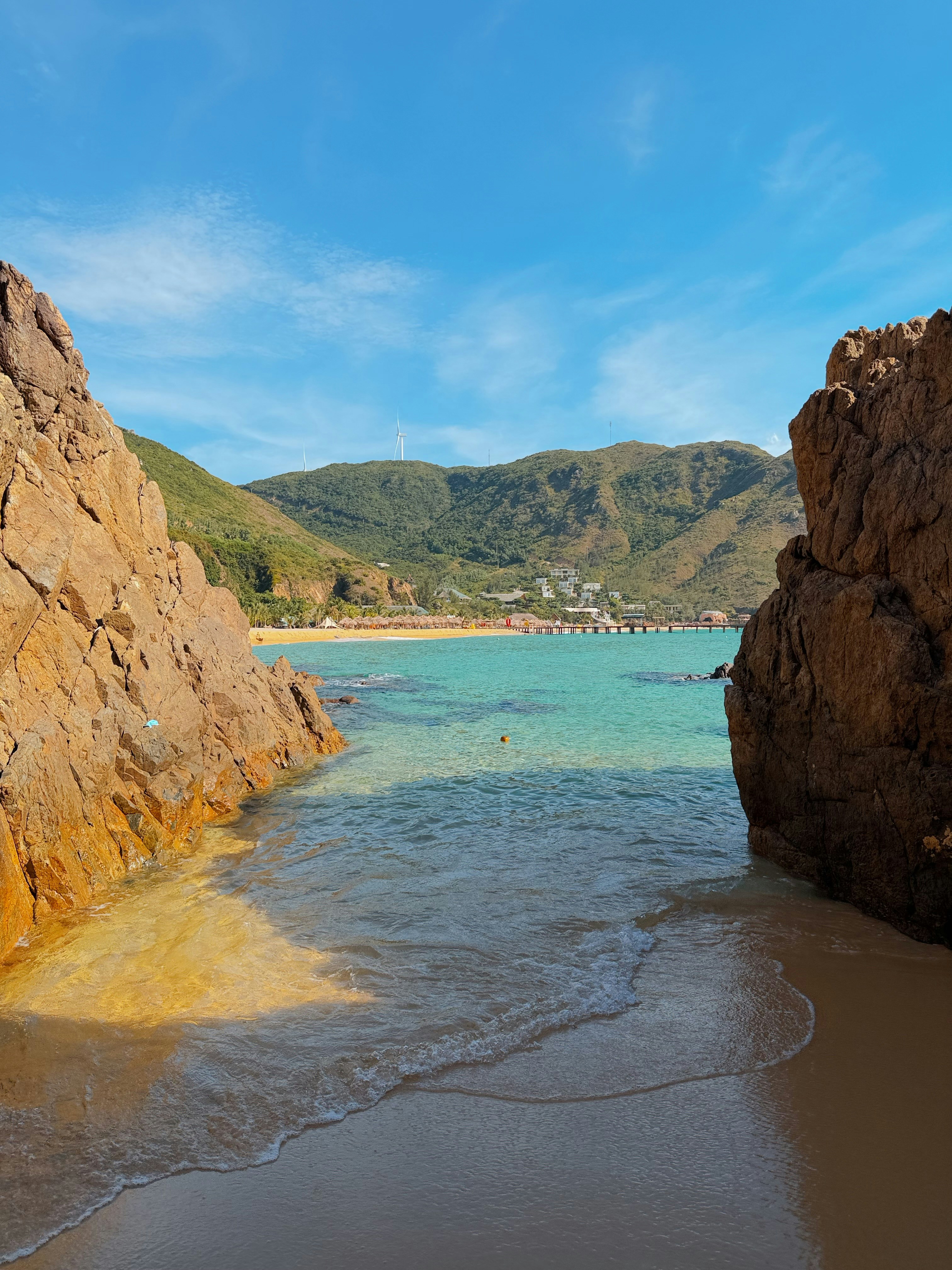 A turquoise bay framed by rocky cliffs with a sandy beach and green hills