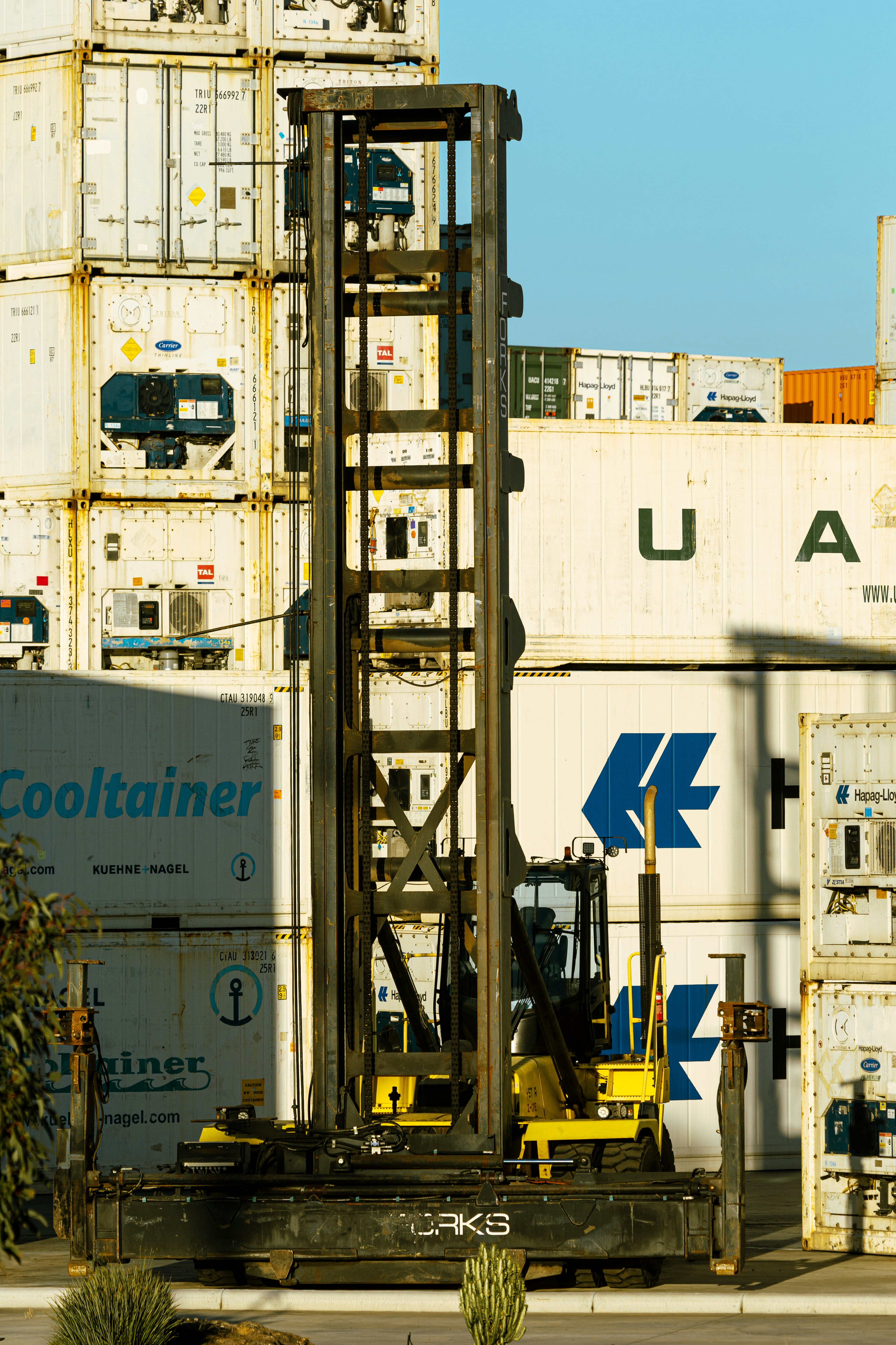 A yellow reach stacker parked in front of stacked white shipping containers