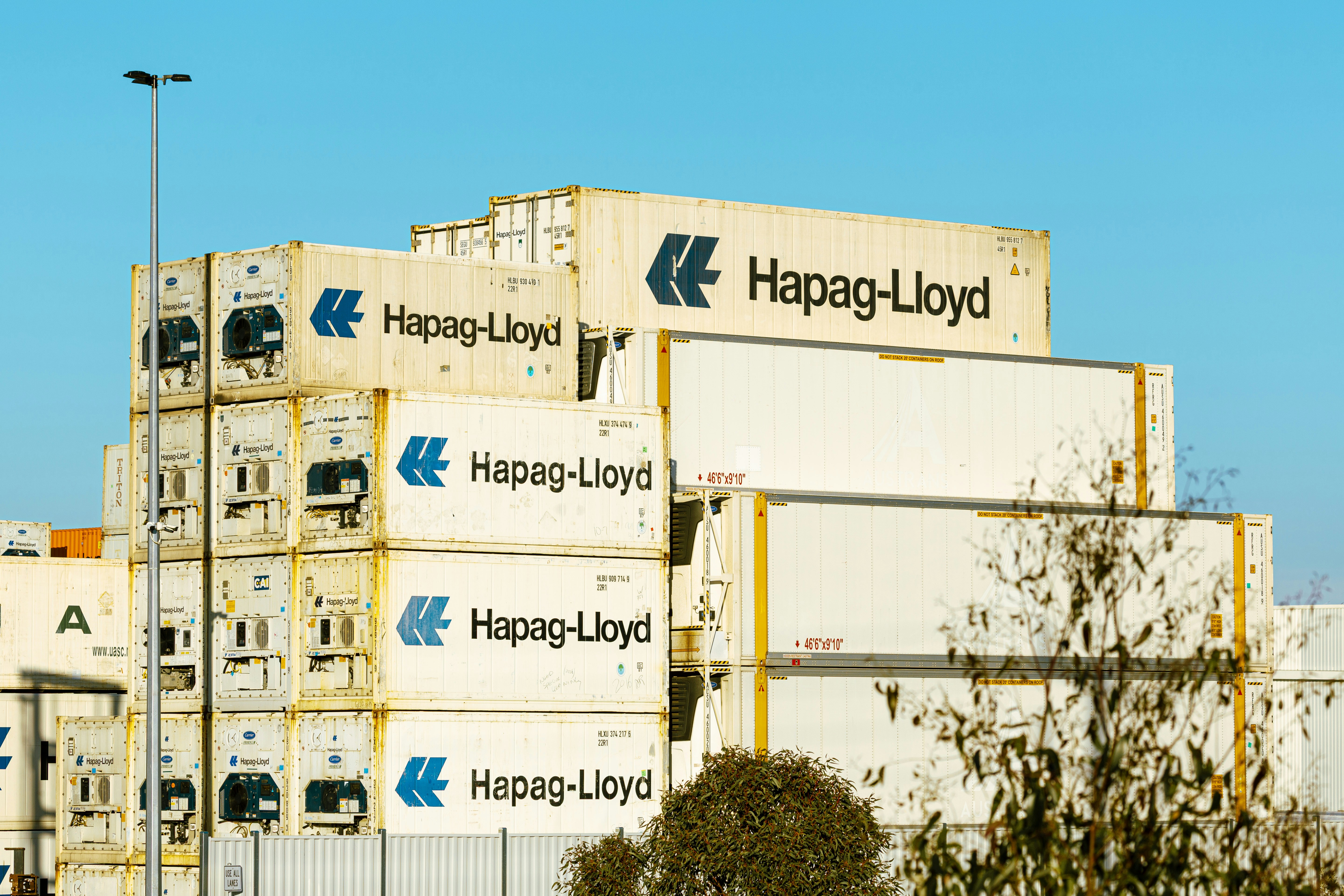 Stacked white Hapag-Lloyd shipping containers against a clear blue sky
