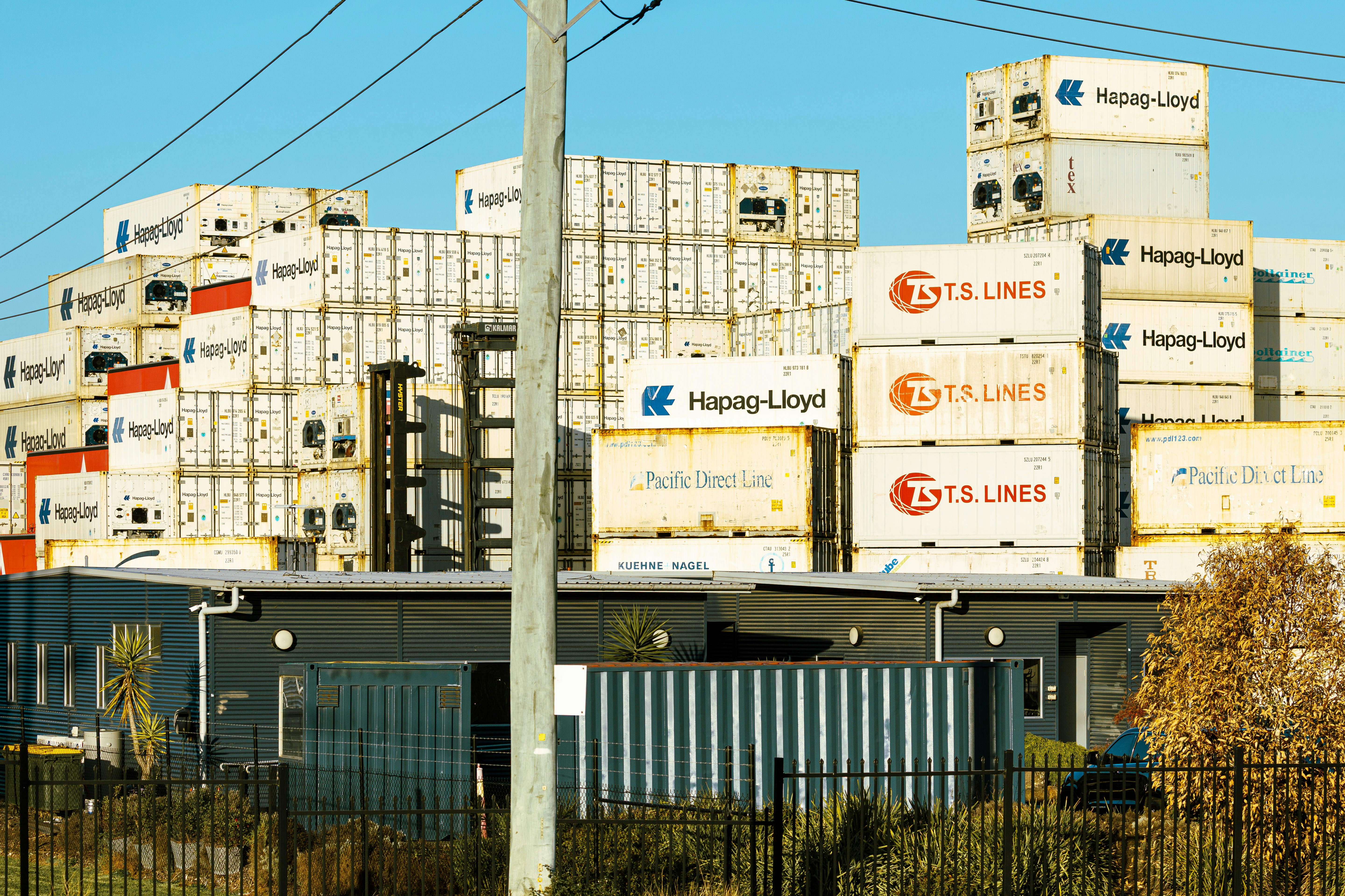 Stacked shipping containers with various company logos behind a dark industrial building