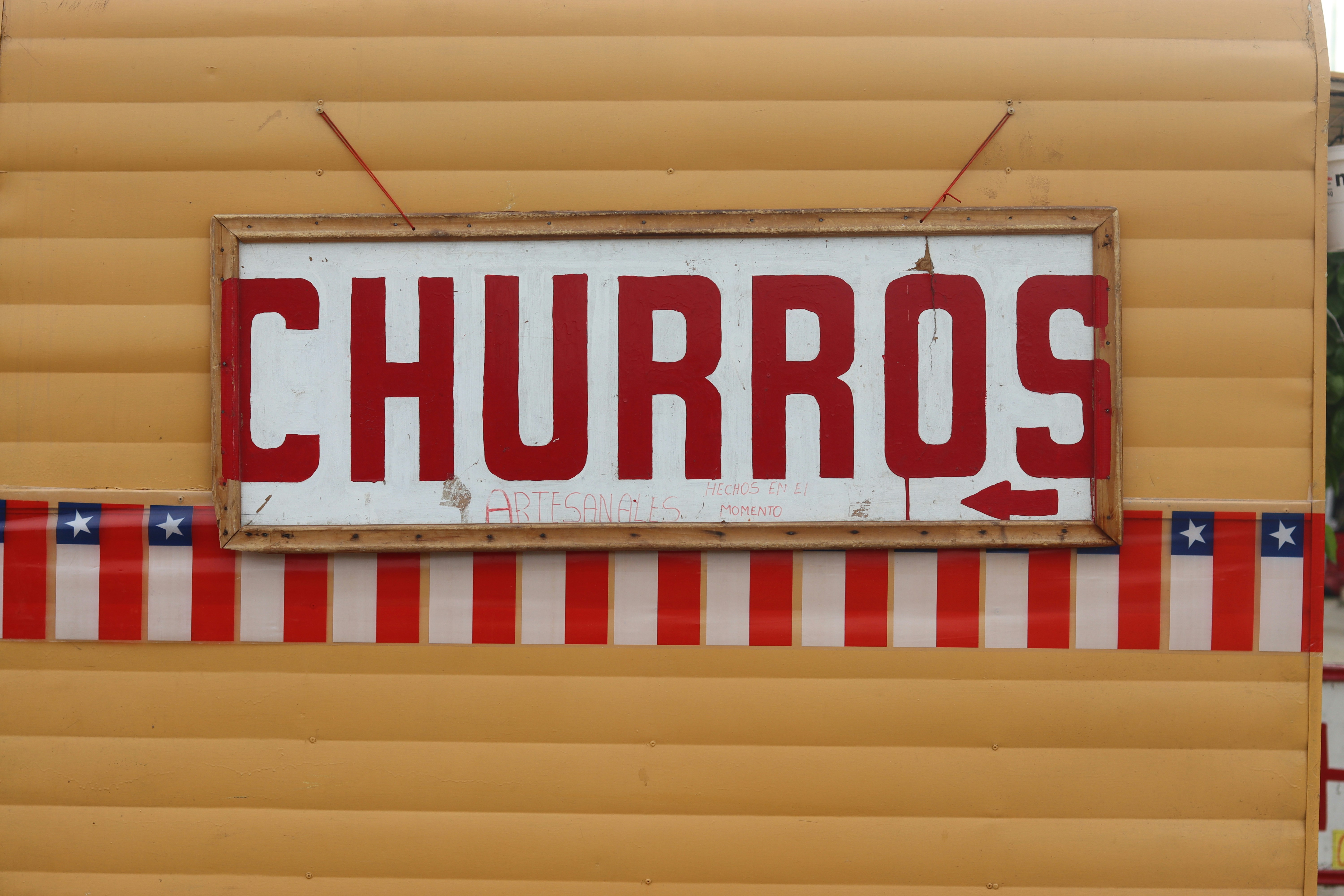 ストライプの縁取りが施された黄色い波板の金属壁に「CHURROS」と書かれた看板