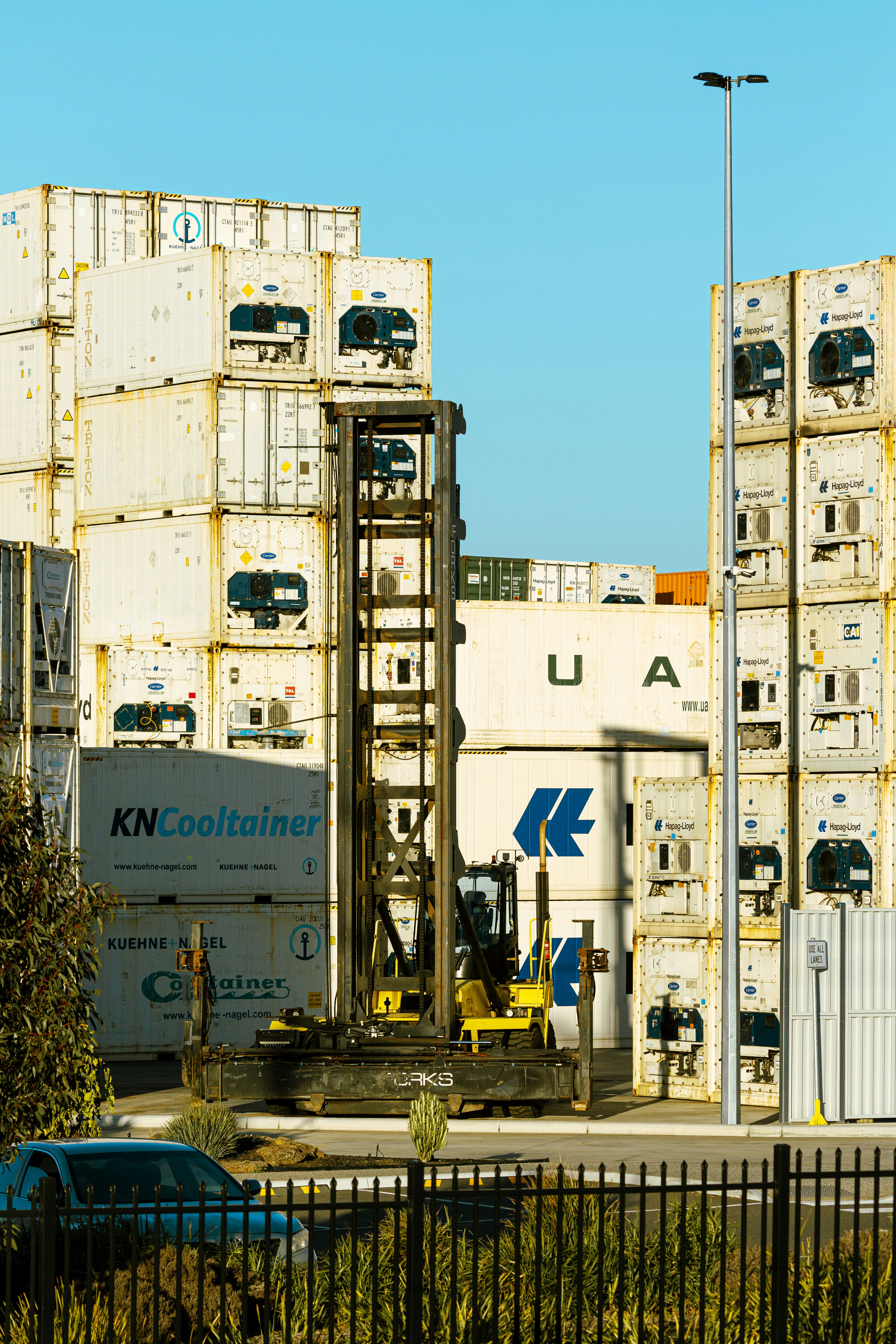 A yellow reach stacker parked in front of stacked white shipping containers