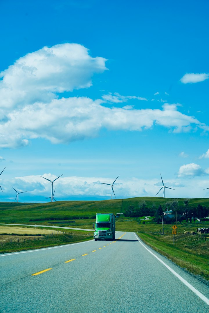 Green semi truck on a rural highway past wind turbines