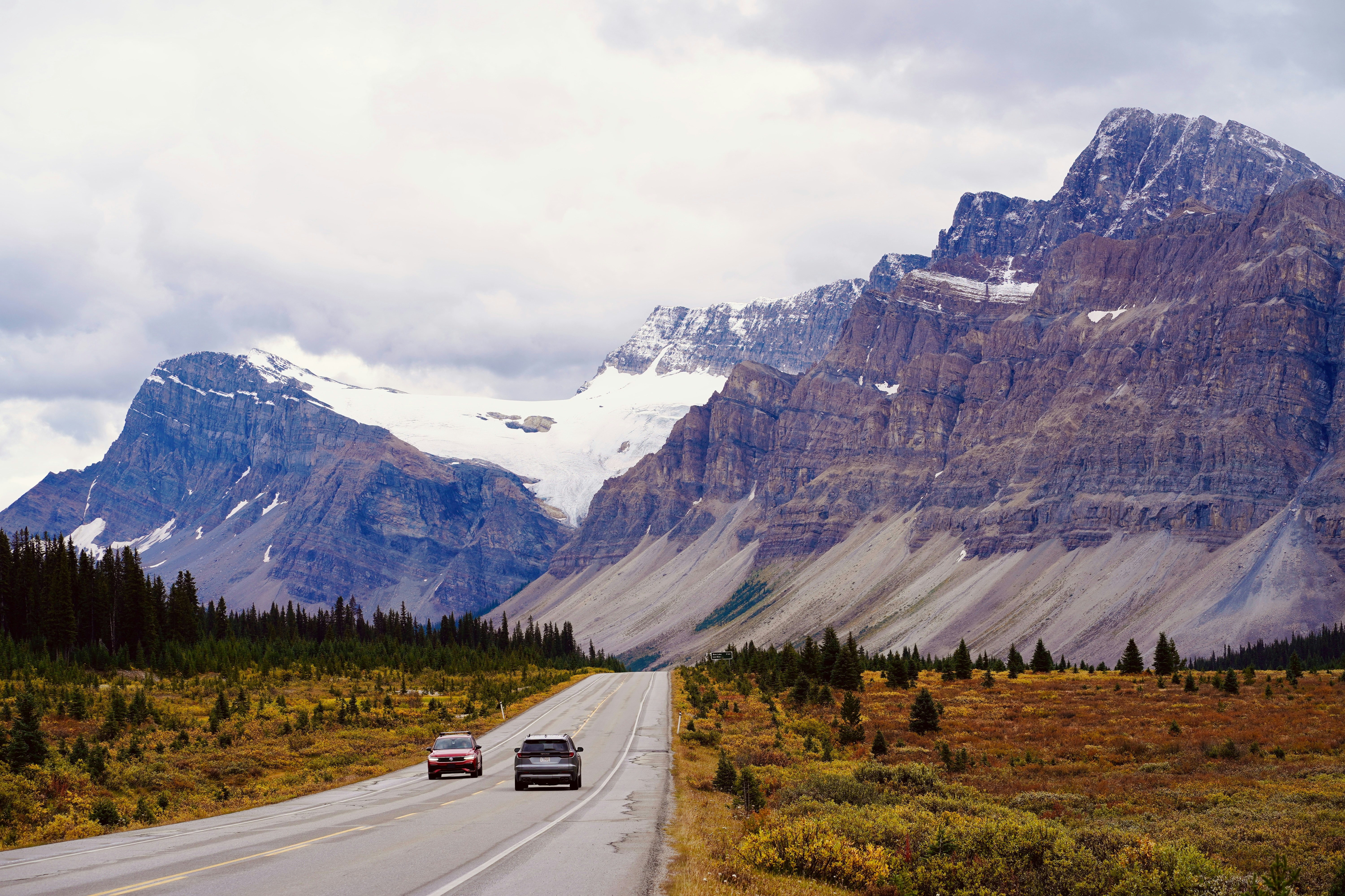 Two cars driving on a road through a valley with large rocky mountains