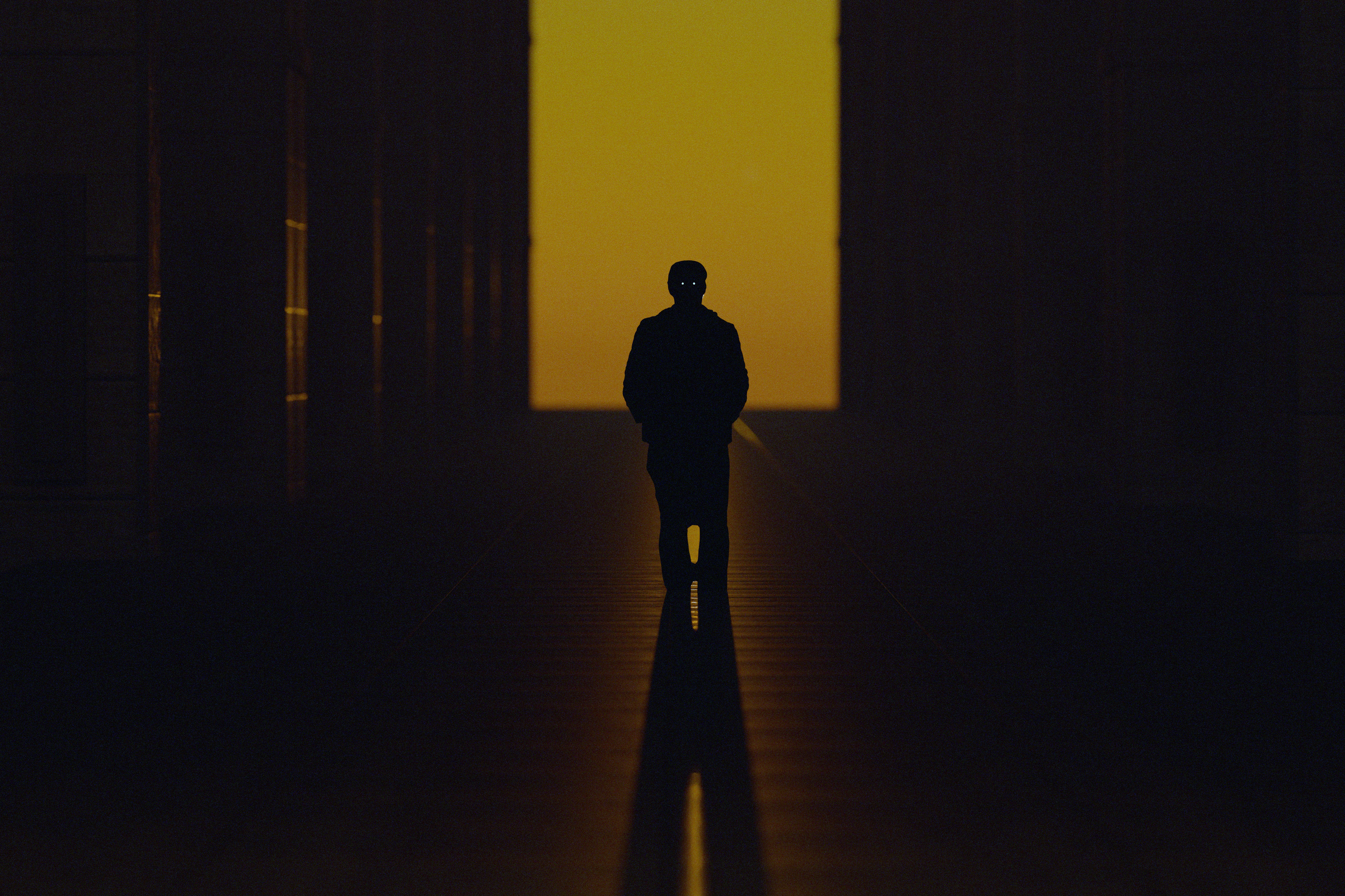 A person in silhouette against a bright yellow rectangular light in a dark corridor