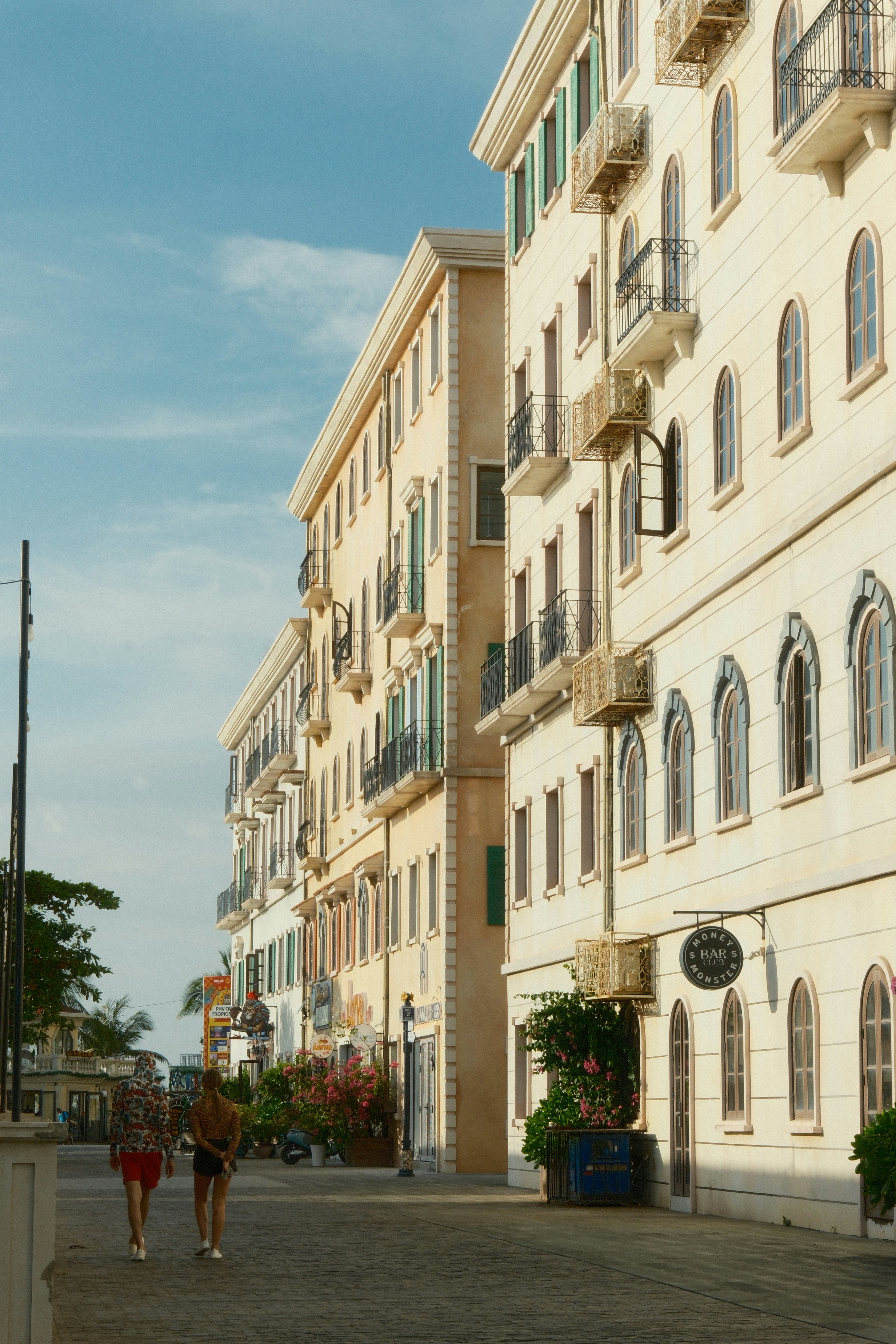 Two people walking down a street lined with tall cream-colored buildings and balconies