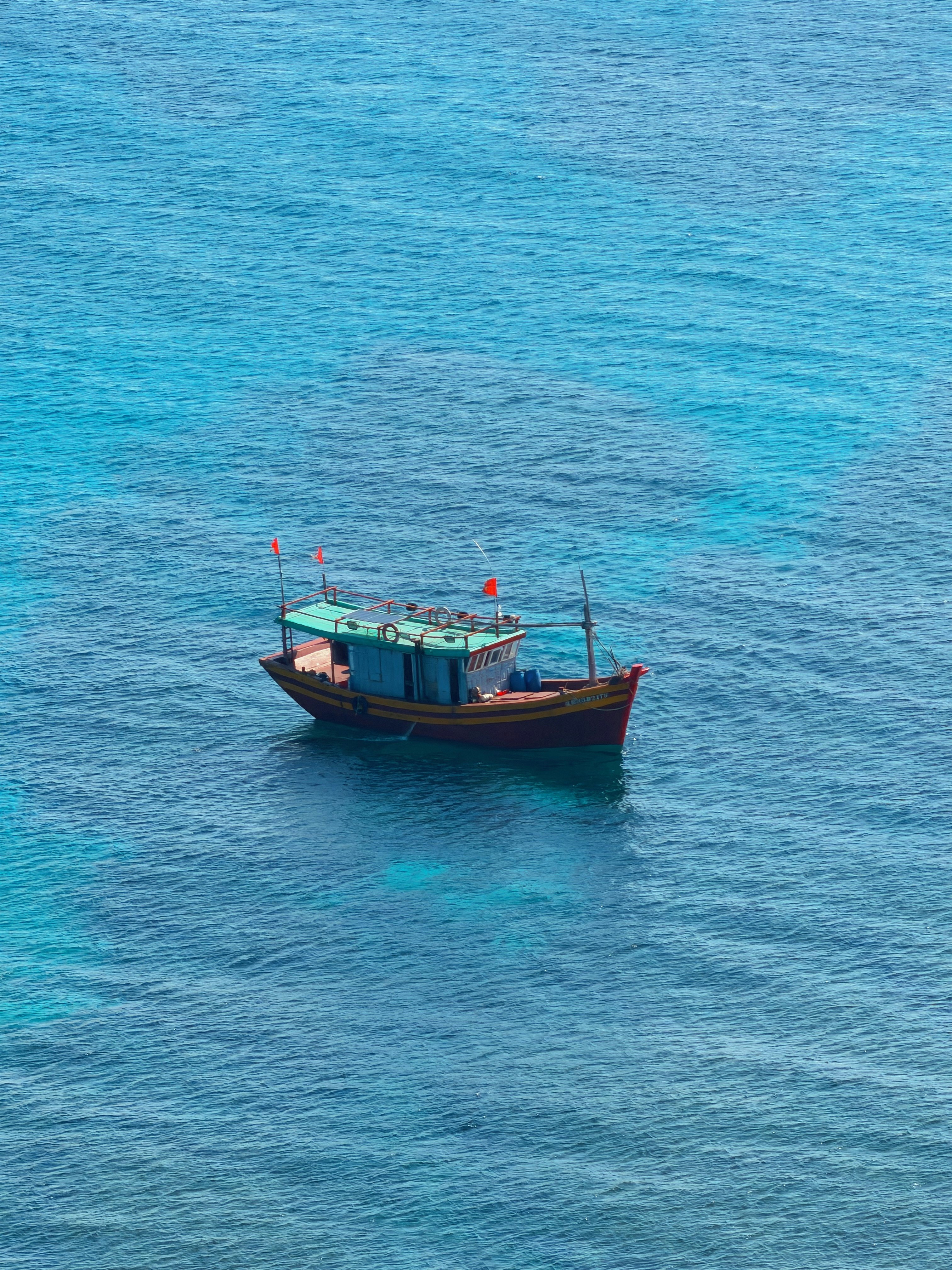 A small wooden fishing boat with red flags on clear blue ocean water