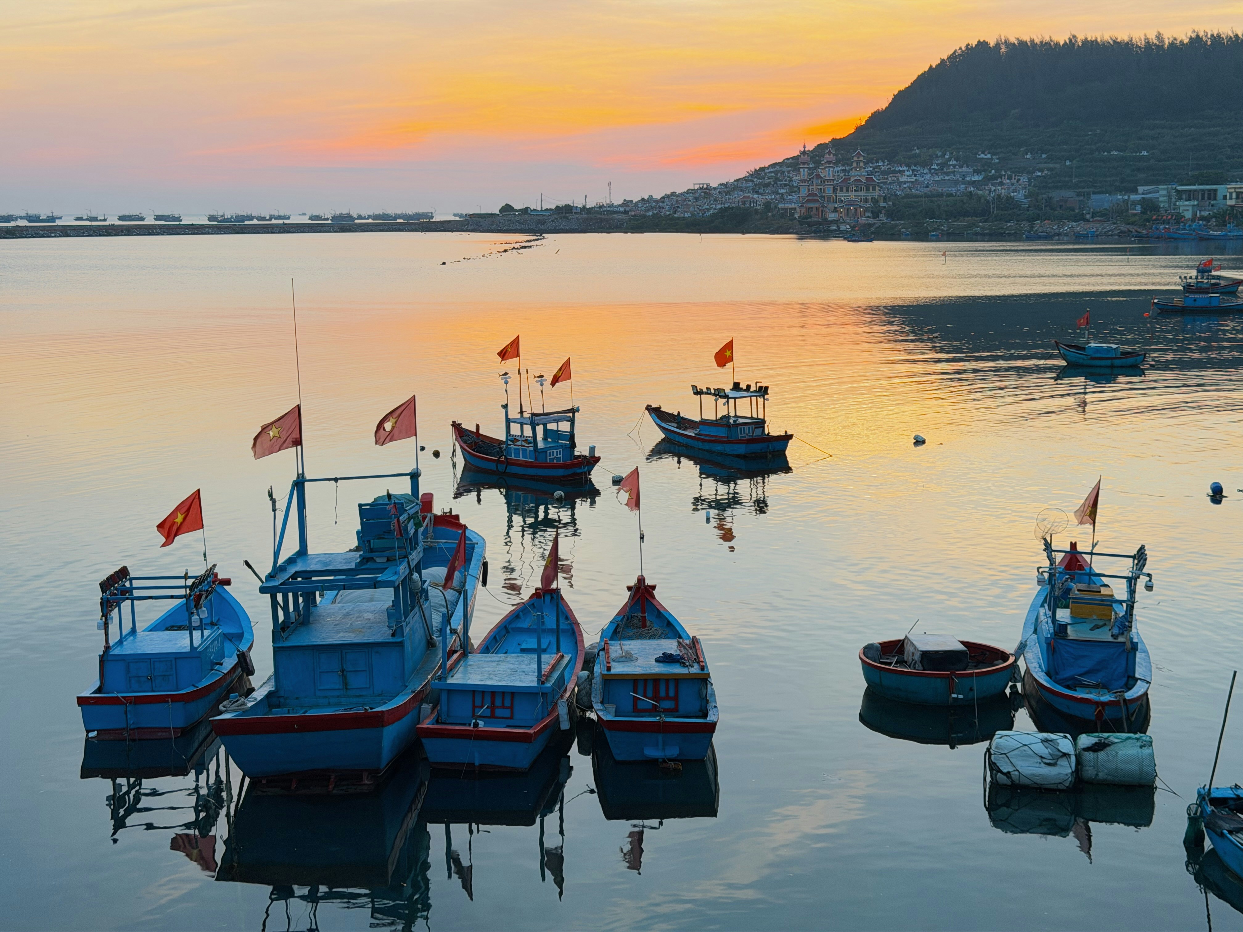 Blue fishing boats with red flags moored in a calm harbor at golden hour